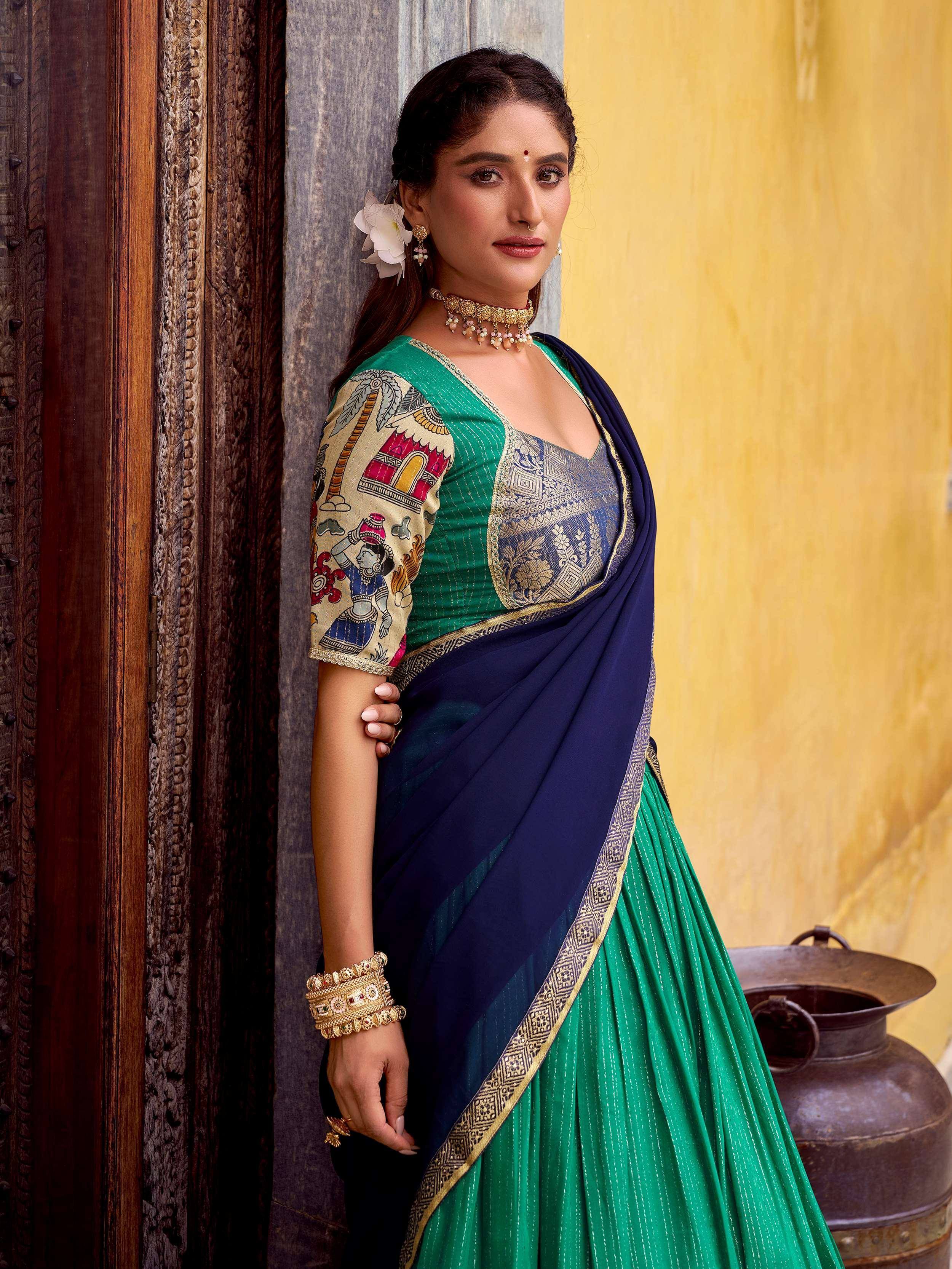 Woman in green and navy blue designer saree with printed blouse, ethnic jewelry, against carved wooden door