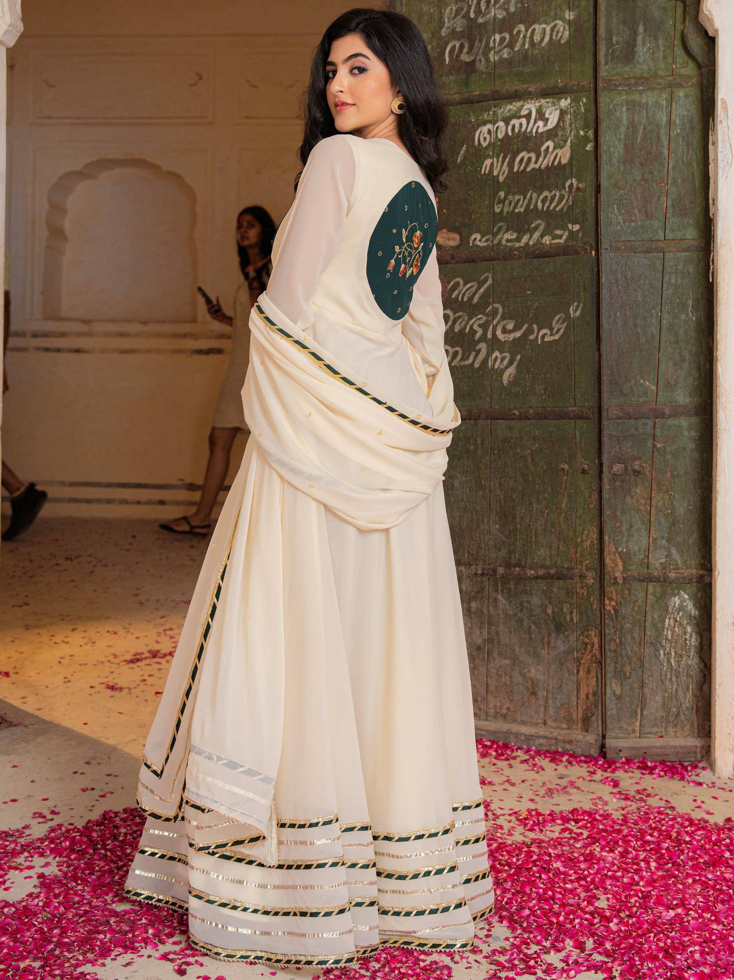 Cream designer lehenga choli with green and gold embroidery, floral motifs, and rose petals on floor
