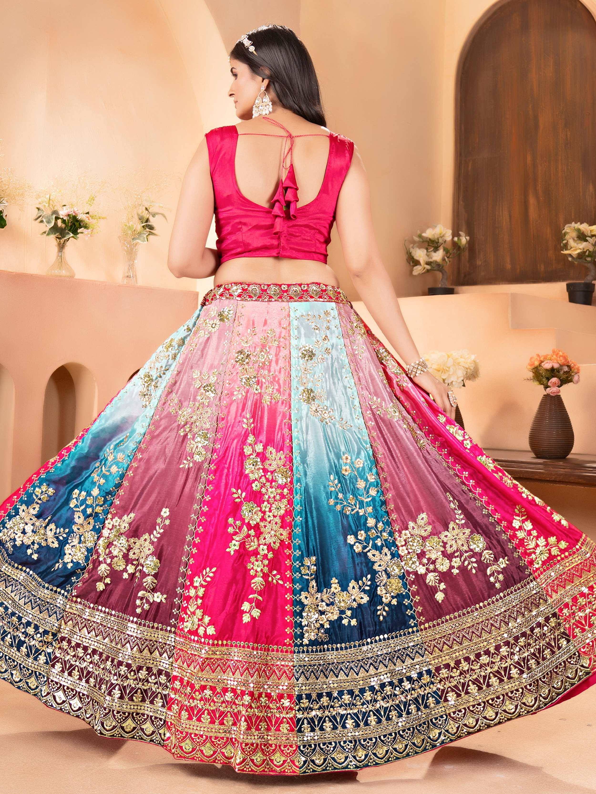 Woman in vibrant pink and blue embroidered lehenga choli with floral motifs and ruffled back blouse