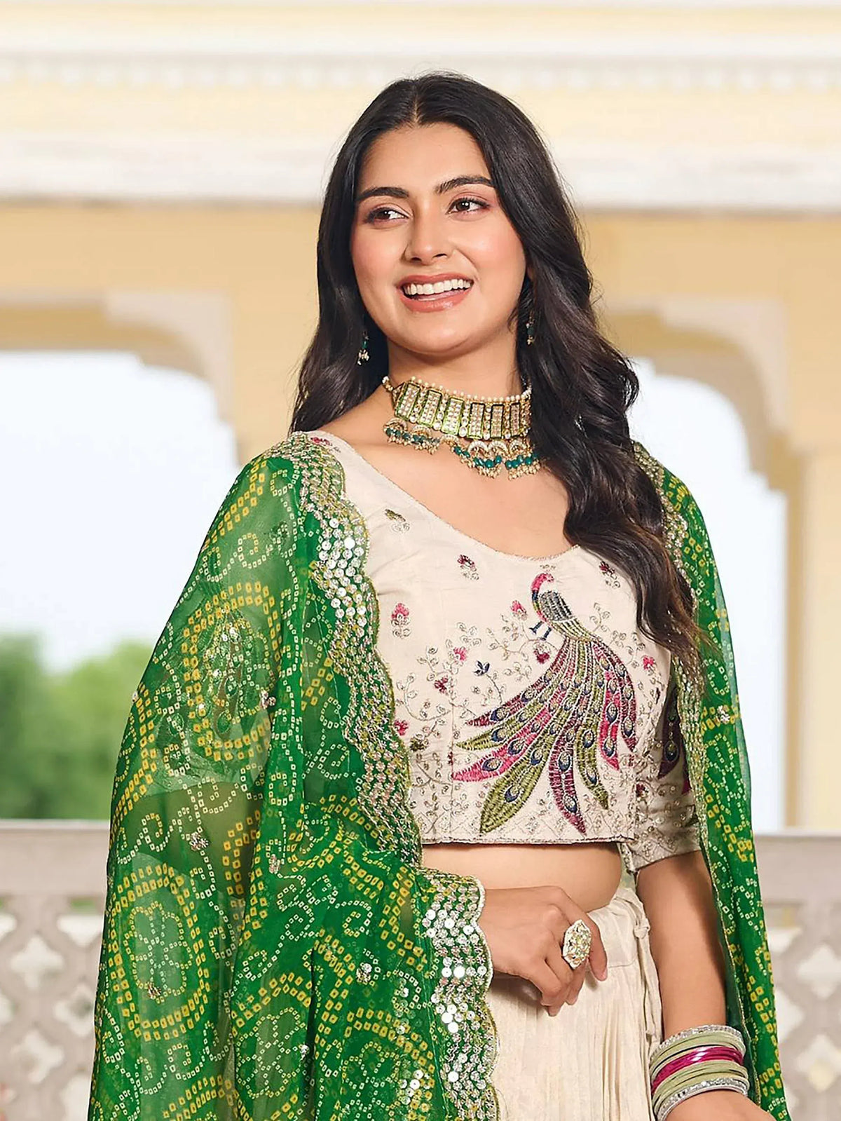 Woman in embroidered beige crop top with peacock design, green patterned dupatta, and ethnic jewelry