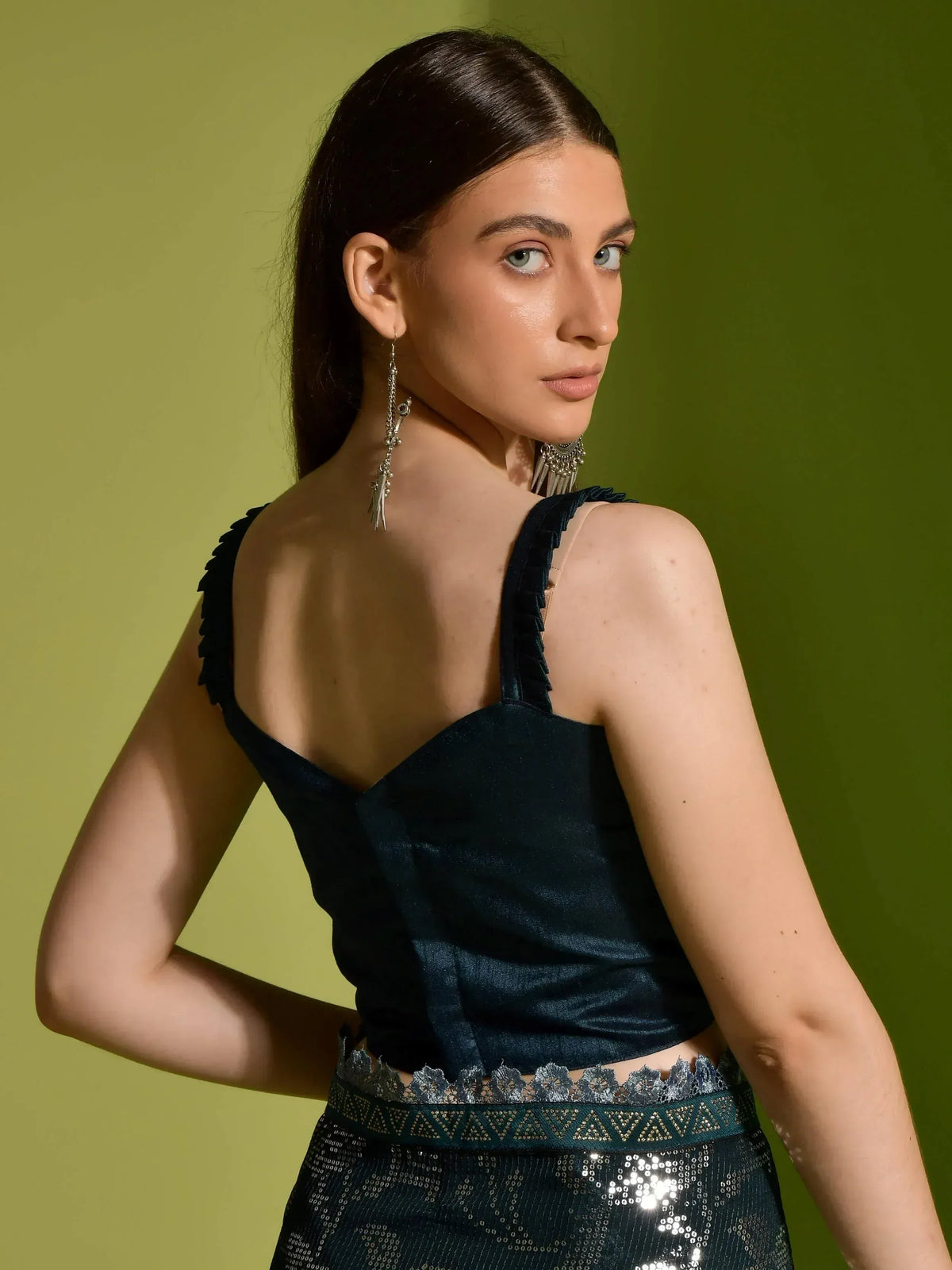 Woman in dark green velvet ethnic top with sequin skirt, showcasing backless design and silver earrings