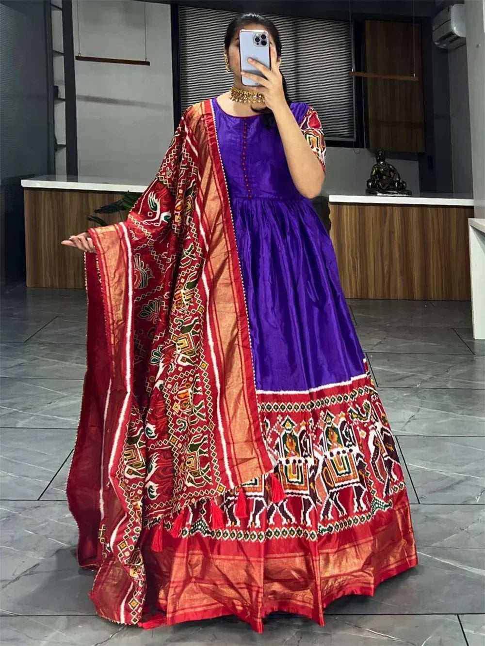 Woman wearing a purple ethnic gown with printed red dupatta and traditional jewelry indoors