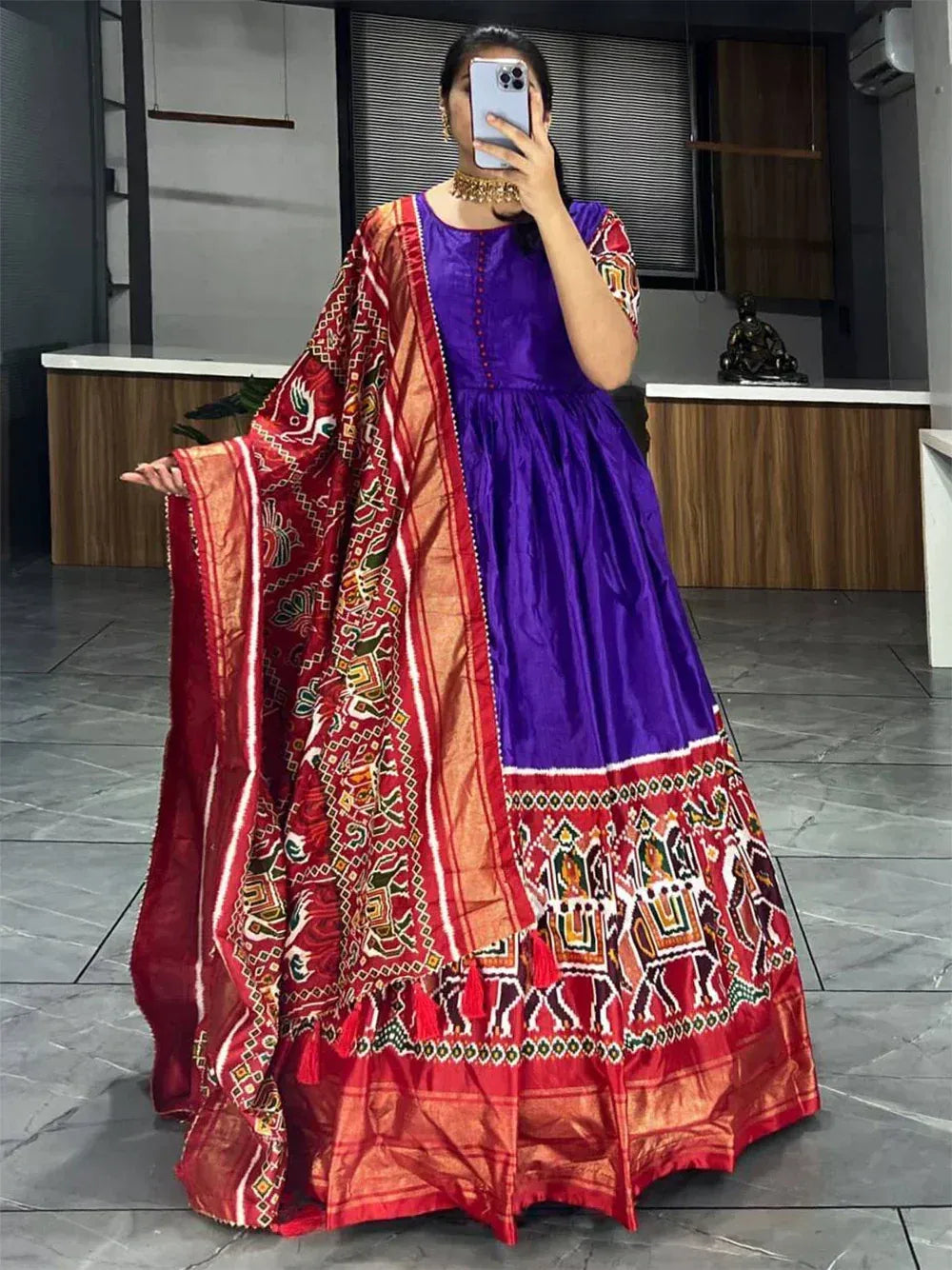 Woman wearing a purple ethnic gown with printed red dupatta and traditional jewelry indoors