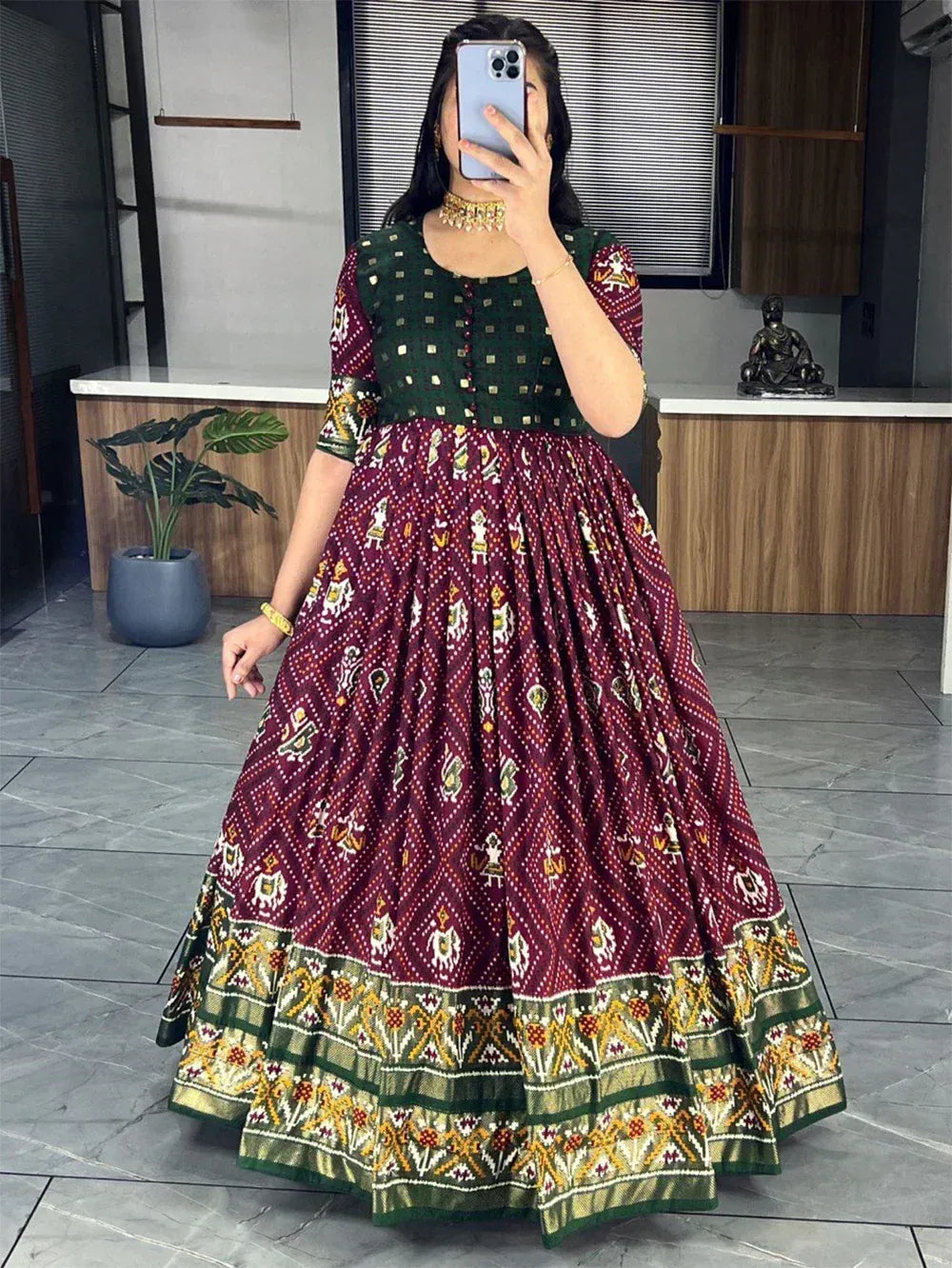 Woman wearing maroon and green printed ethnic gown with traditional motifs in modern interior.