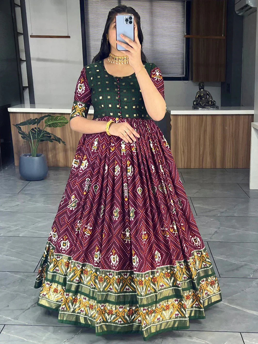 Woman wearing maroon printed ethnic gown with green yoke and gold border in modern room