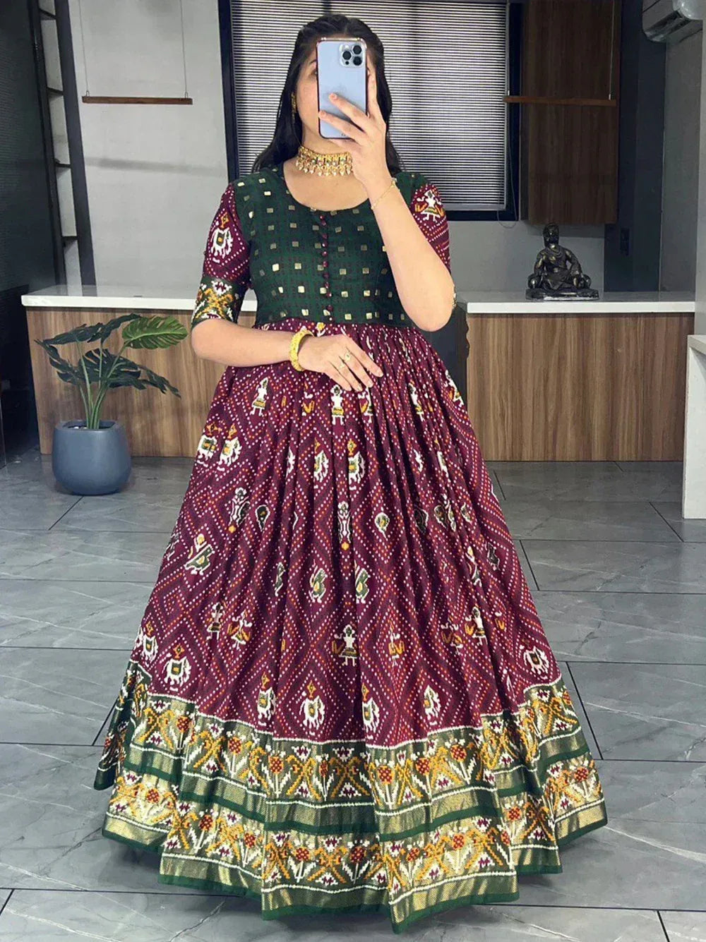 Woman wearing maroon printed ethnic gown with green yoke and gold border in modern room