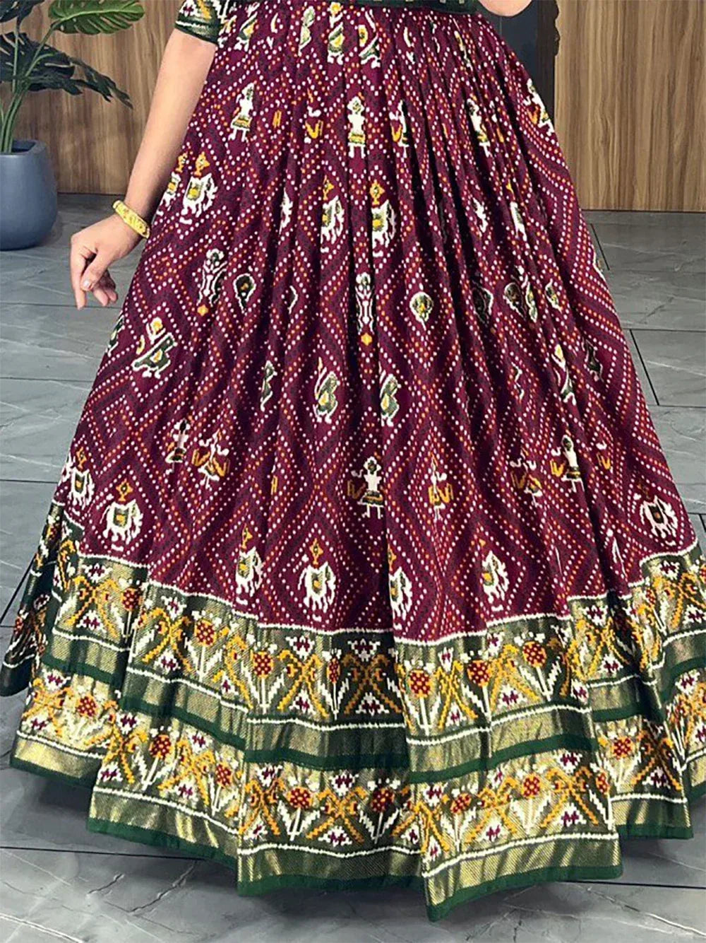 Maroon ethnic lehenga with traditional bandhani print, green gold border, and colorful motifs