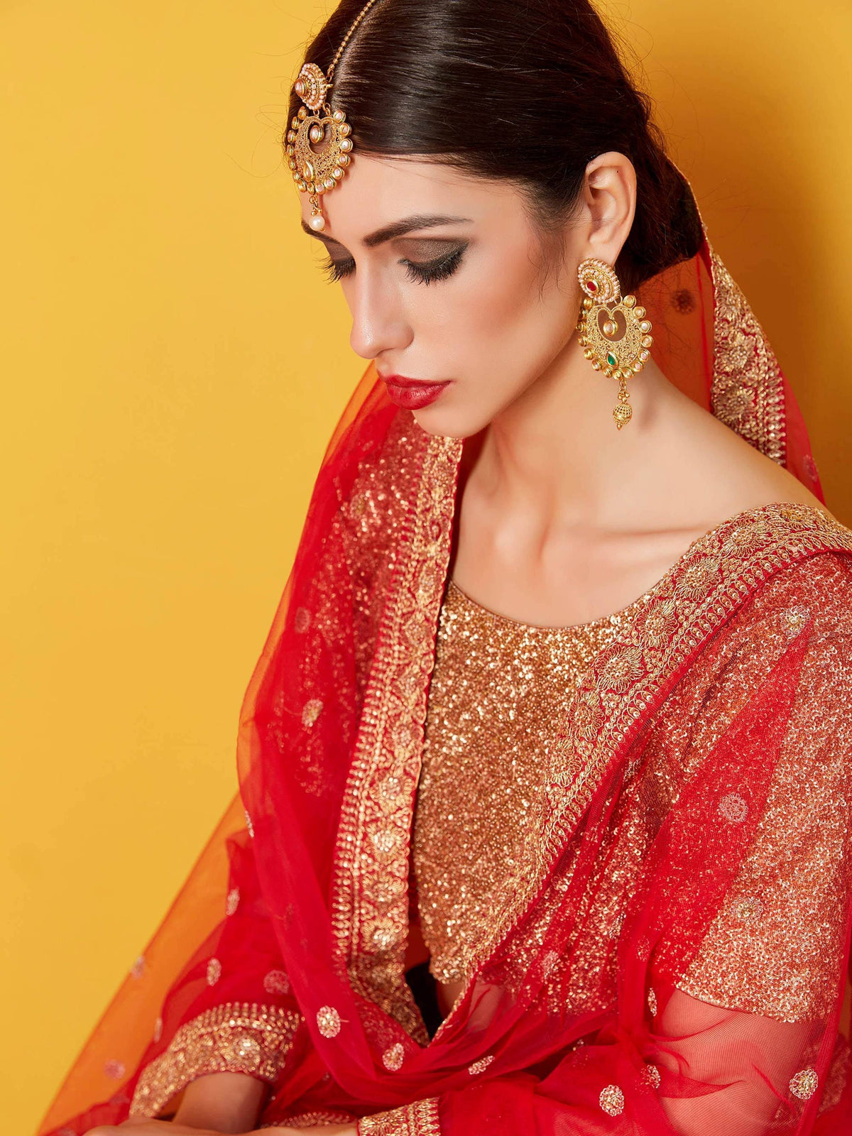 Red and gold embroidered Indian bridal lehenga with matching jewelry and dupatta
