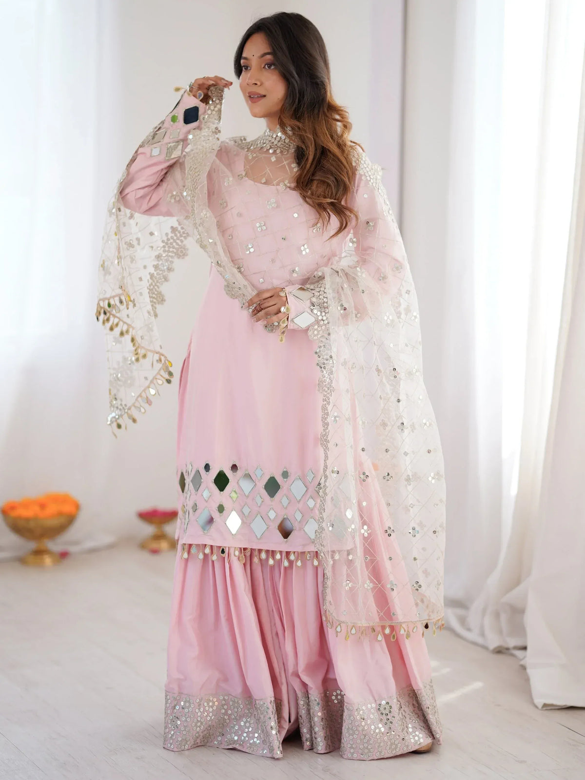 Woman wearing a baby pink mirror-work salwar kameez with a matching embellished dupatta