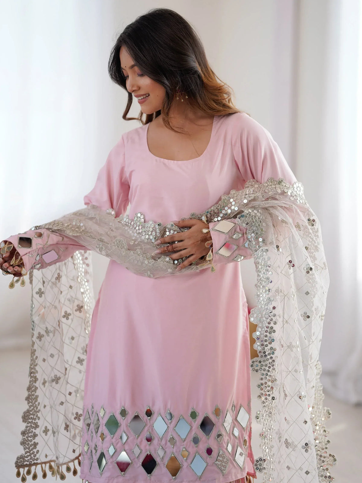 Woman wearing a pink salwar kameez with mirror work detailing and a matching dupatta.