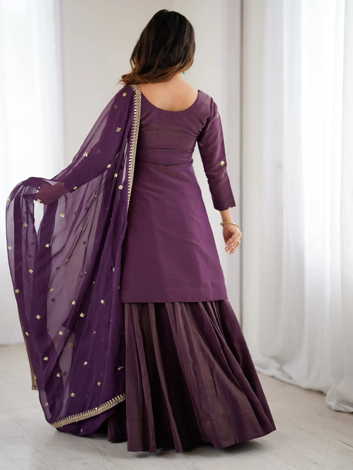 Back view of a woman wearing a purple Indian ethnic salwar kameez with a matching dupatta.
