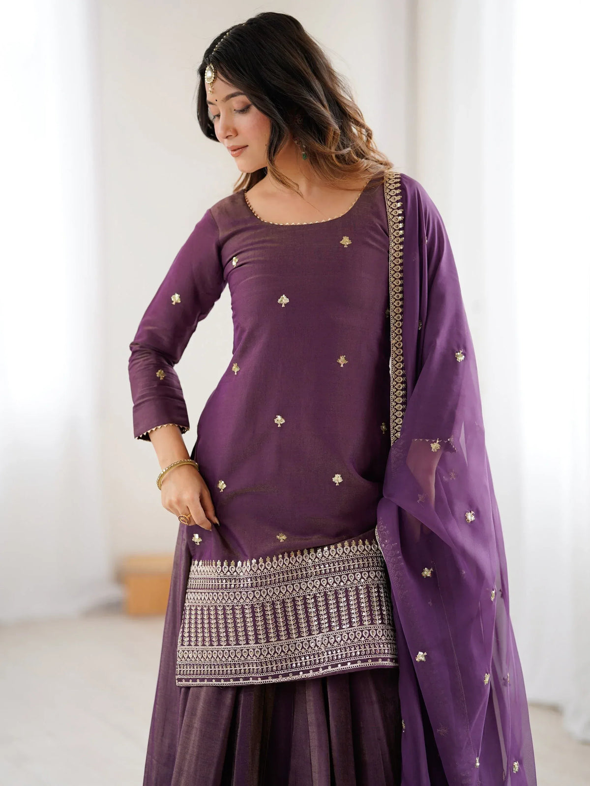 Woman wearing a purple designer salwar kameez with gold embroidery and a matching dupatta.