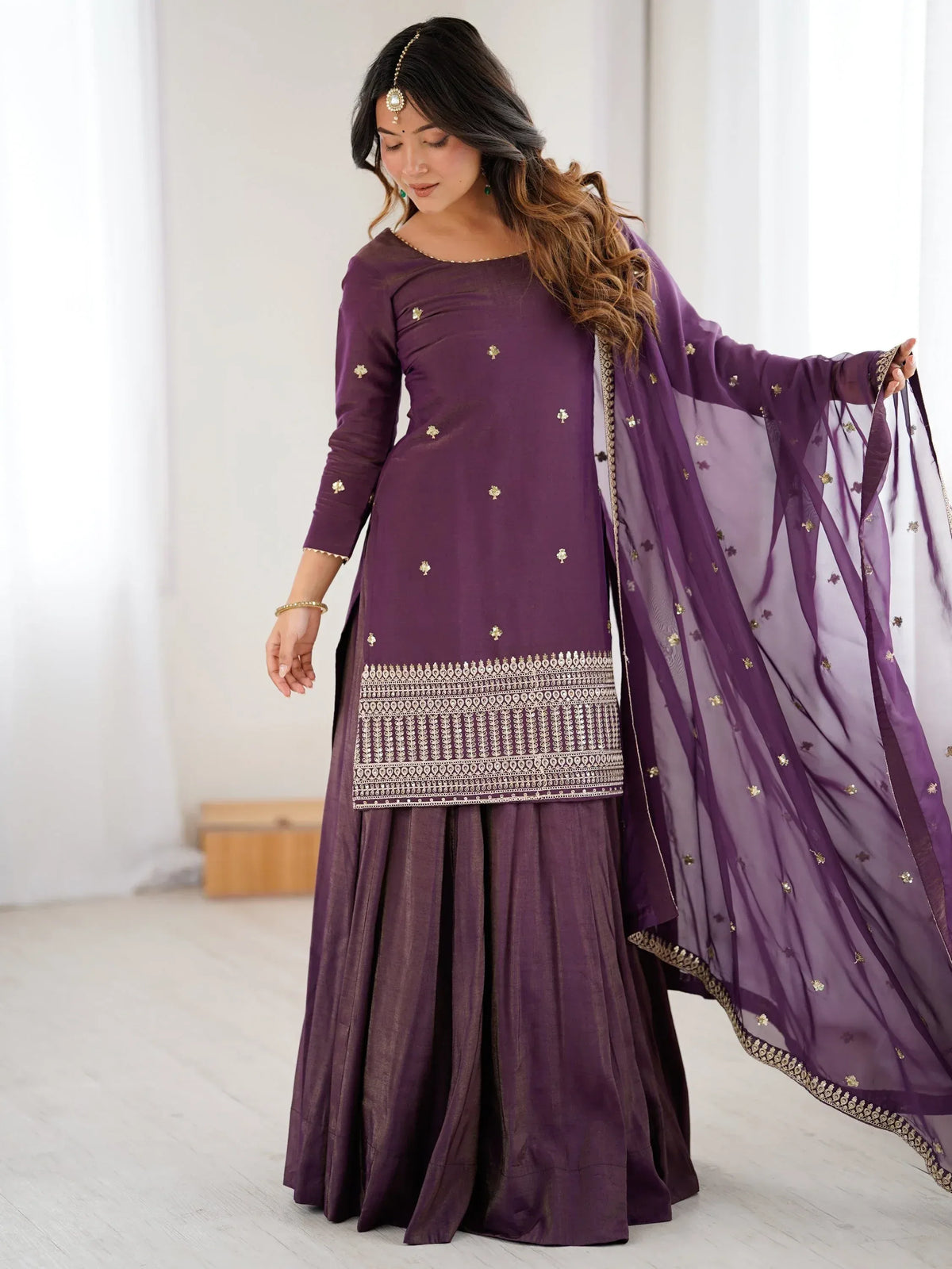 Woman wearing a purple designer salwar kameez with gold embroidery and matching dupatta