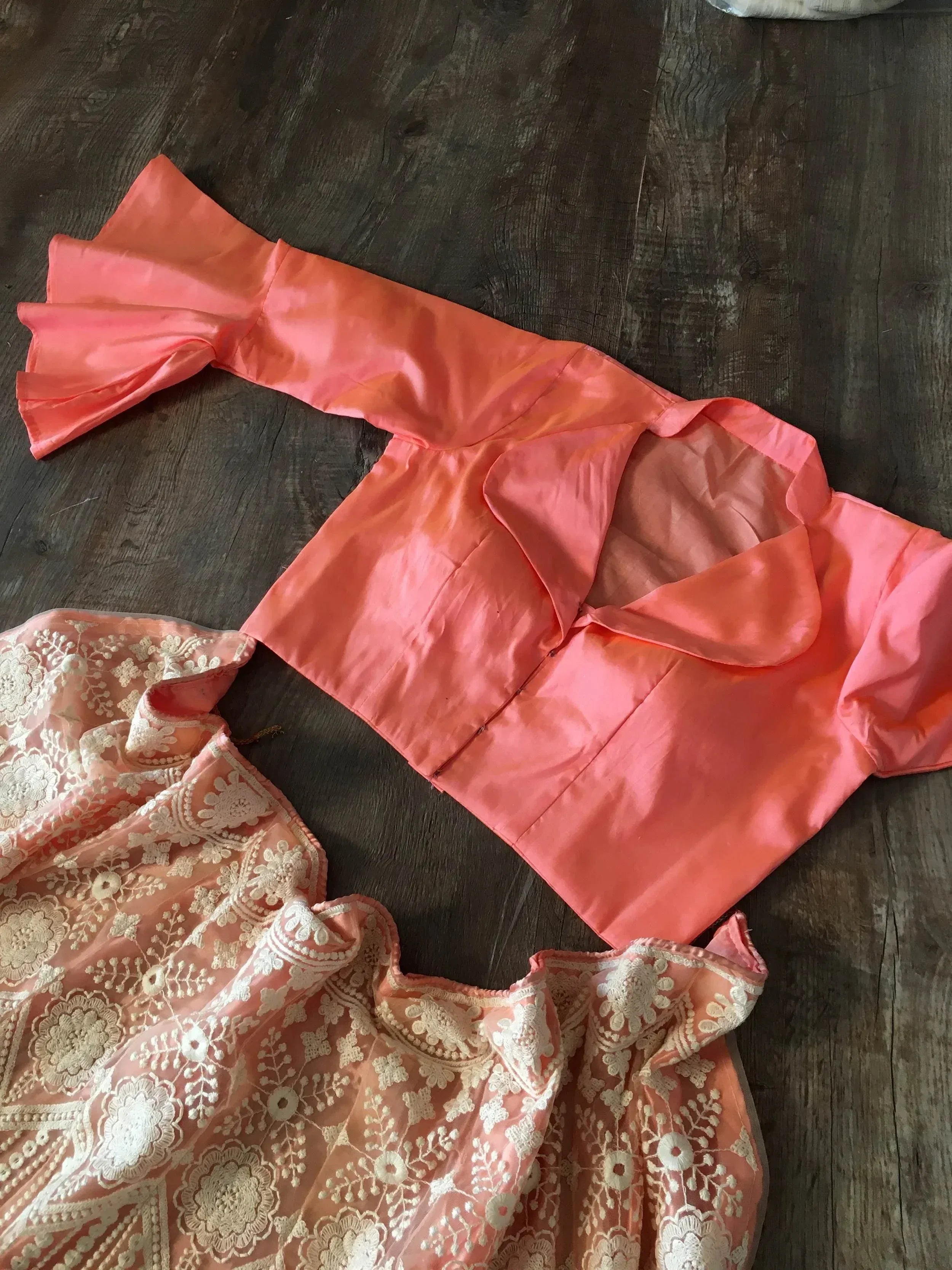 Coral ethnic blouse with bell sleeves and embroidered peach lehenga skirt on wooden floor