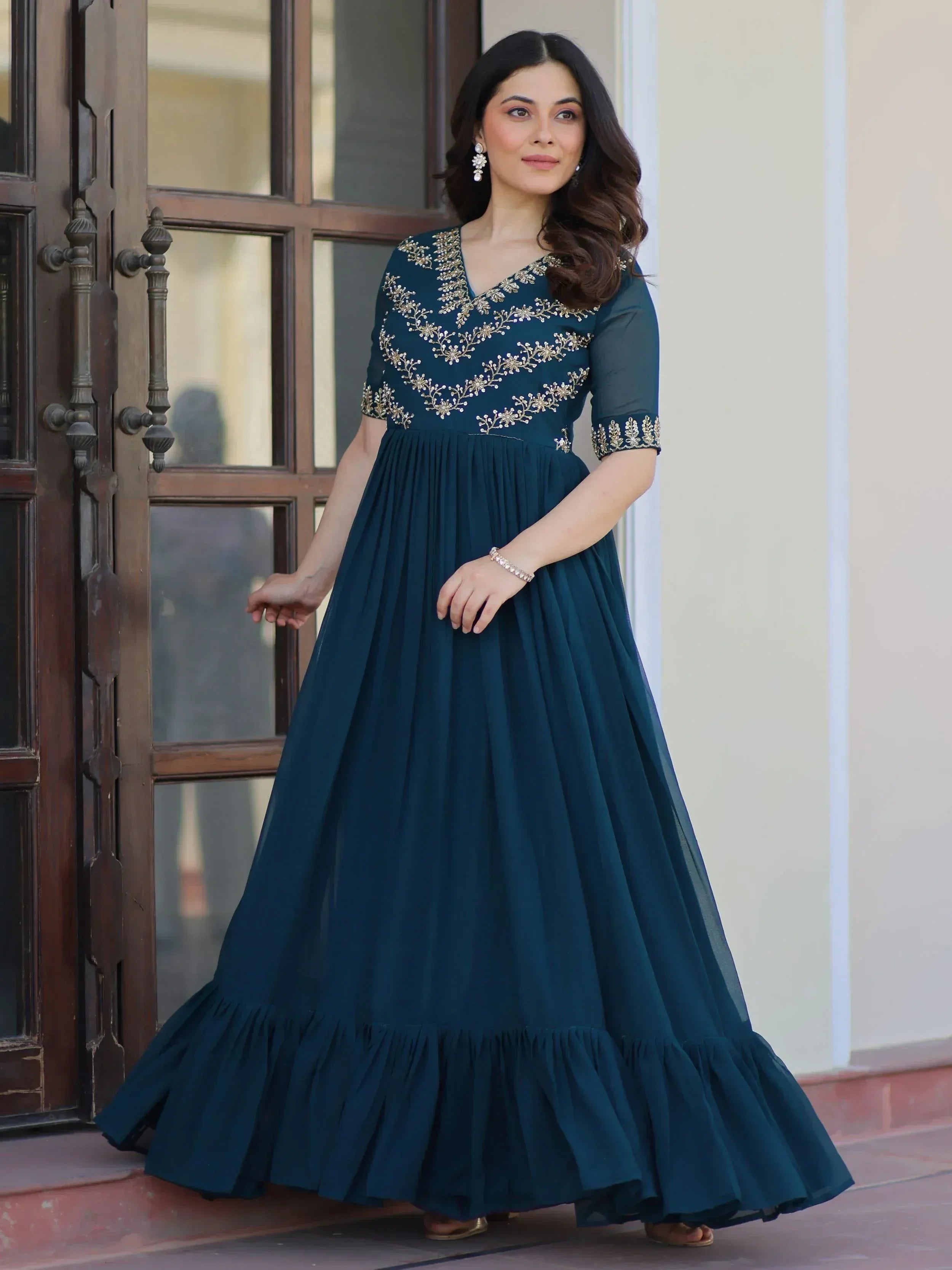 Teal ethnic gown with gold embroidery, pleated skirt, and ruffle hem for Indian occasions
