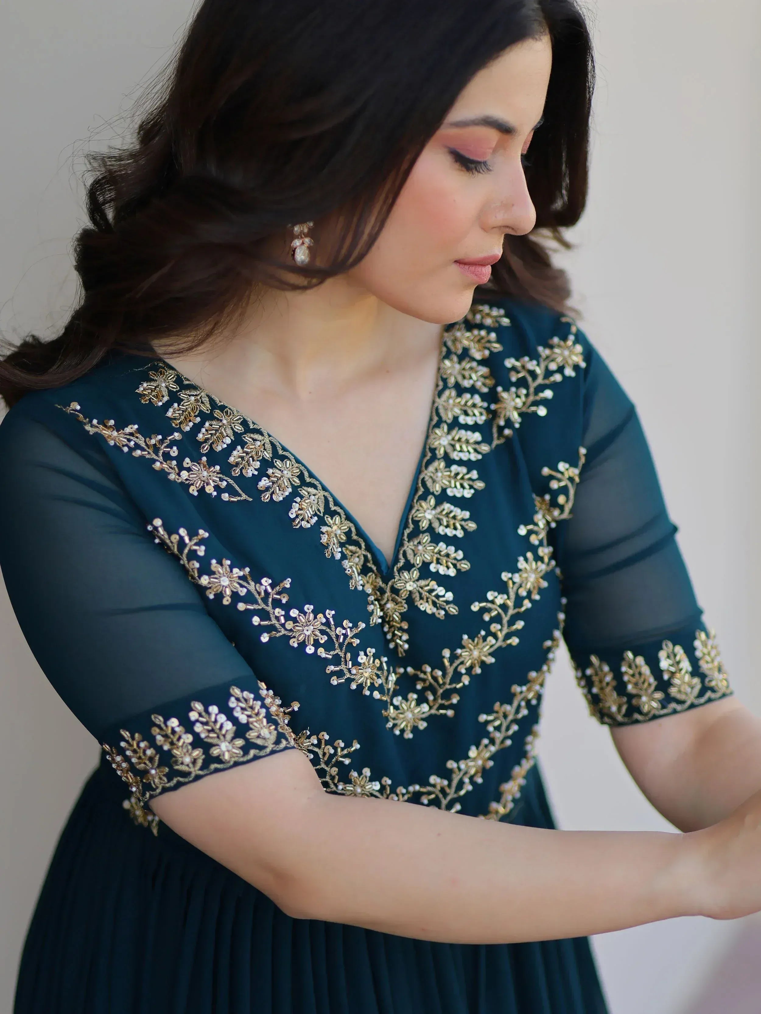 Teal ethnic gown with gold floral embroidery, sheer sleeves, and V-neckline for Indian occasions