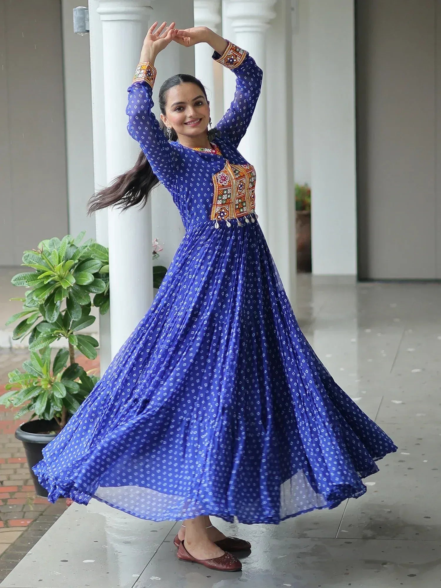 Woman in blue printed ethnic gown with embroidered yoke, twirling outdoors near white pillars