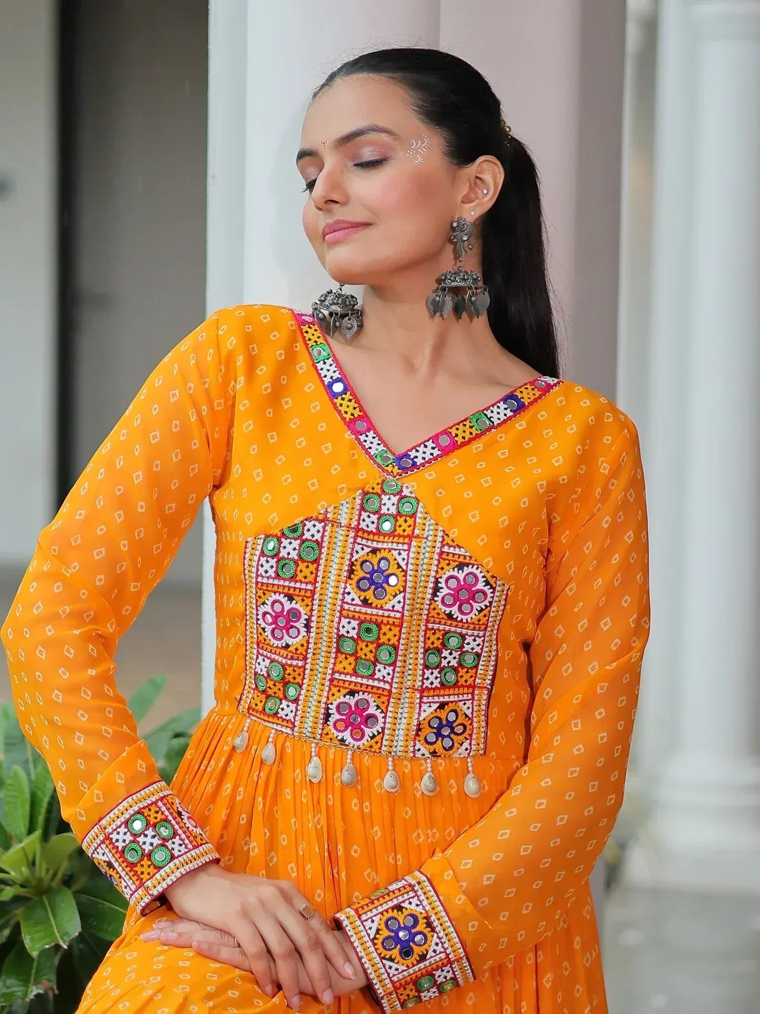 Vibrant orange ethnic gown with mirror work and floral embroidery, perfect for festive occasions.