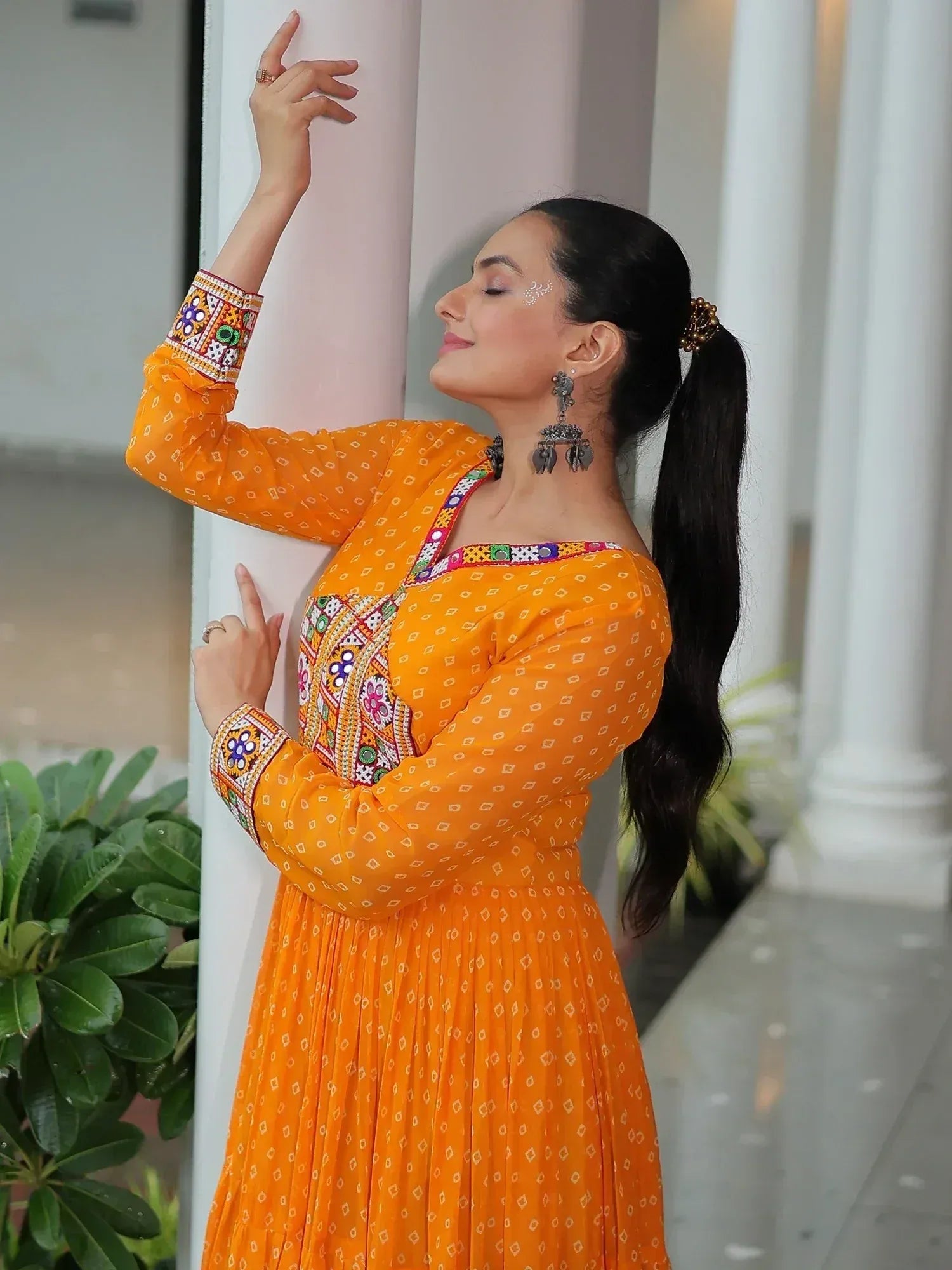 Woman in vibrant orange ethnic gown with colorful embroidery, perfect for Indian festive occasions.
