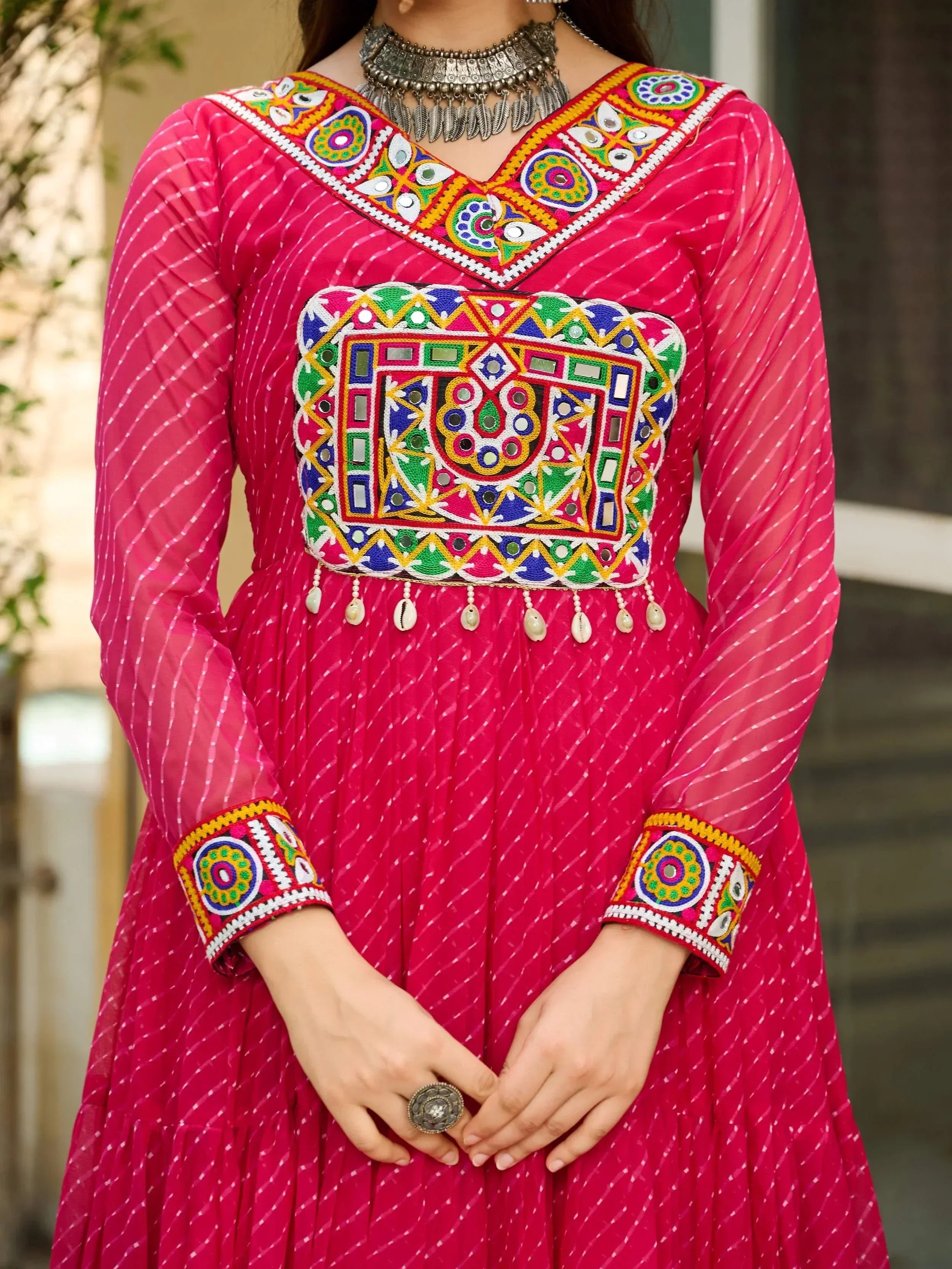 Pink ethnic anarkali with mirror work, embroidery, and shell tassels, paired with silver jewelry