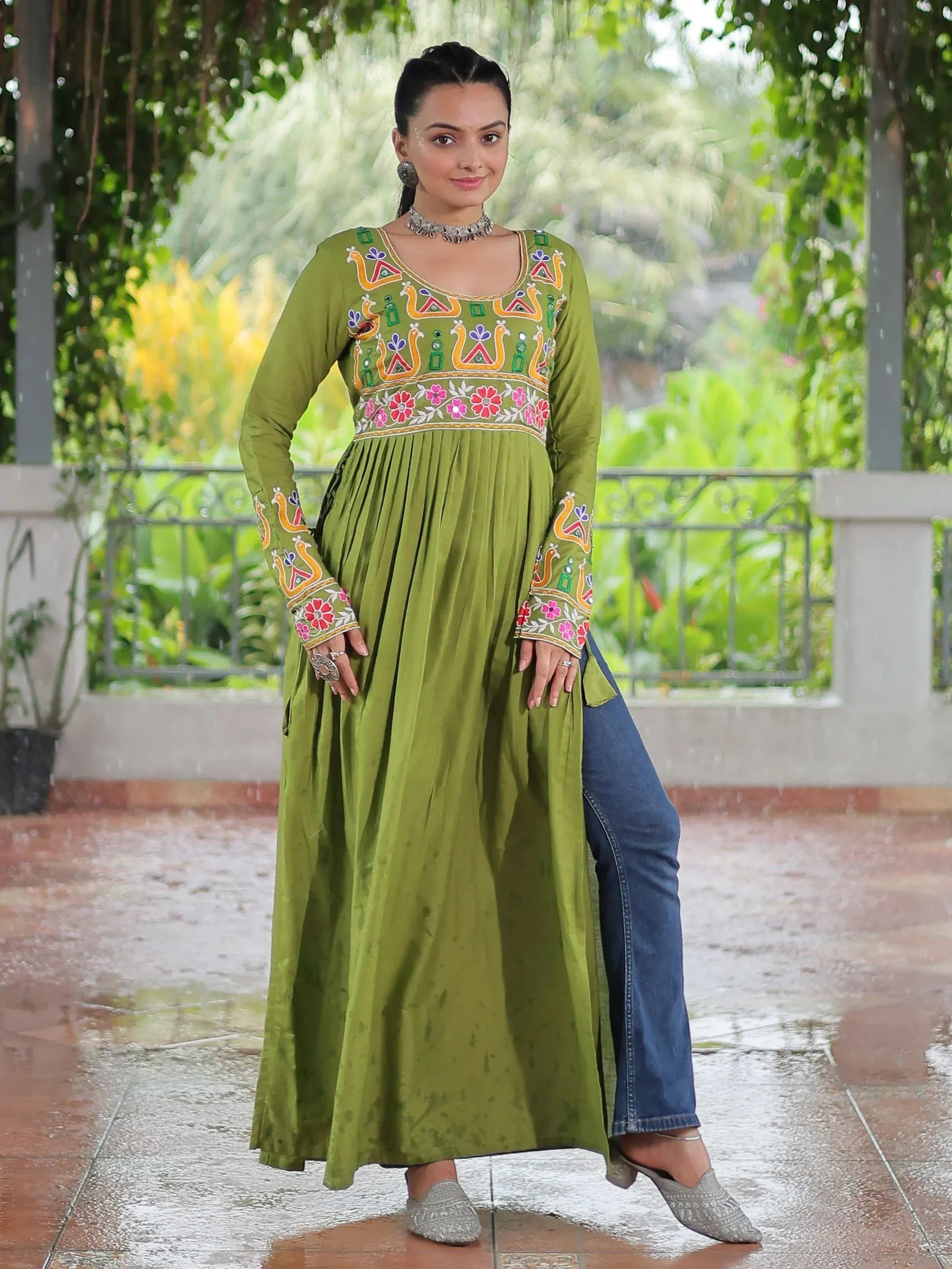 Green embroidered ethnic gown with floral and peacock motifs, paired with jeans and juttis for a fusion look