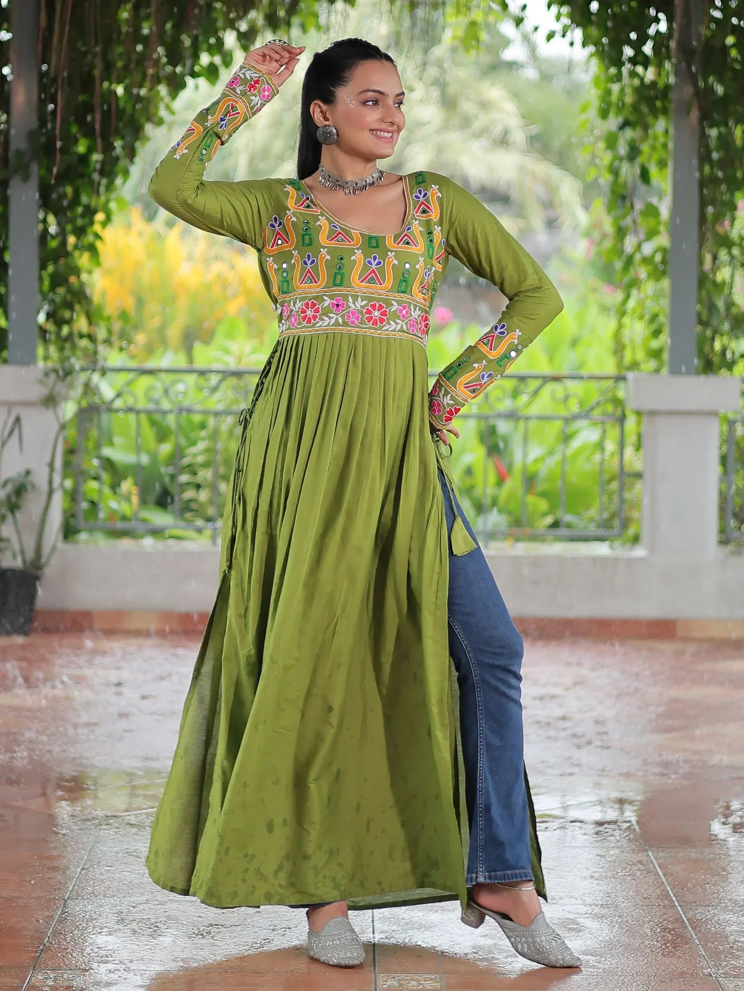 Green embroidered ethnic gown with floral motifs, paired with jeans, for festive or casual wear.