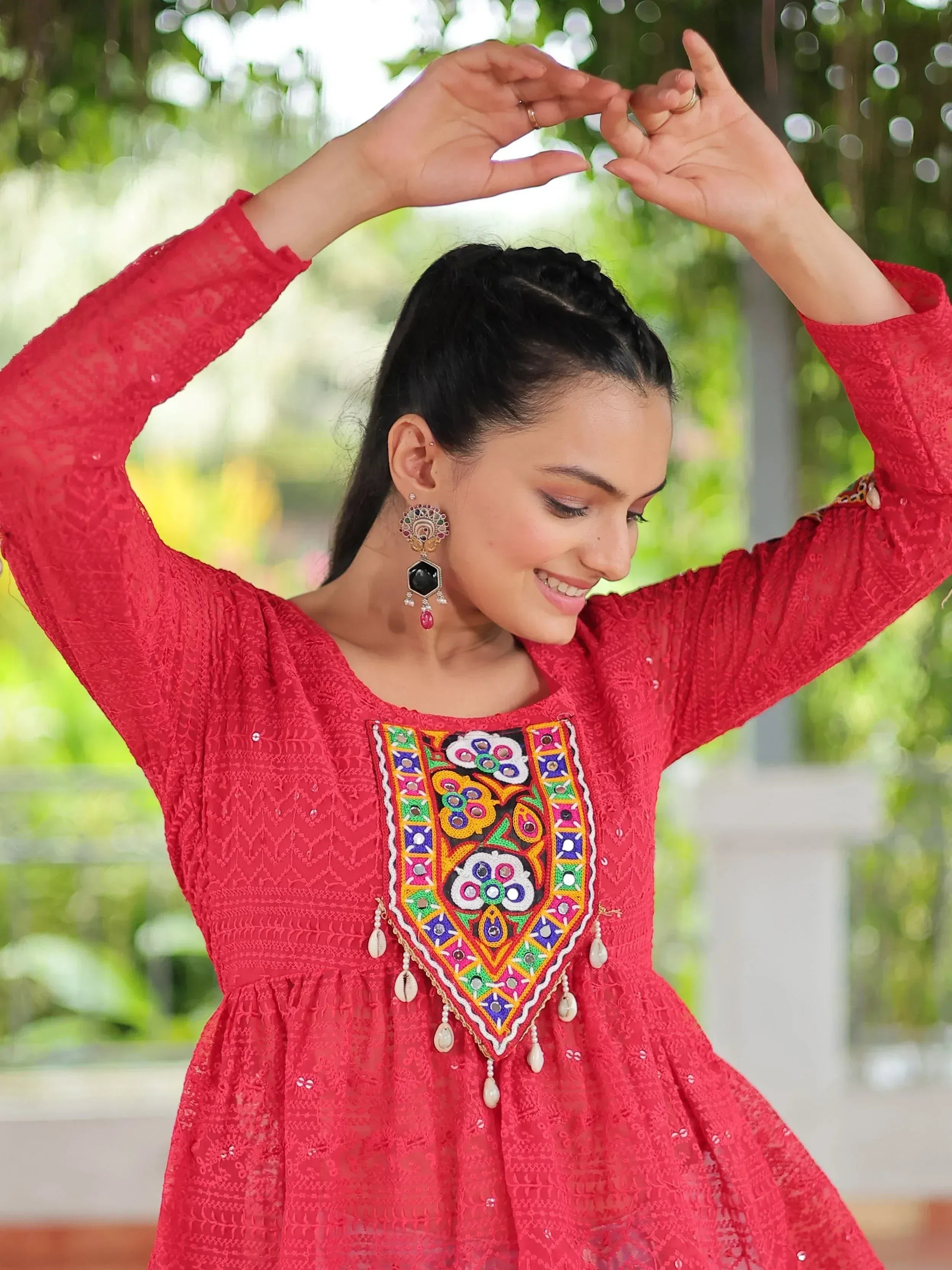 Red embroidered ethnic gown with colorful mirror work and pearl tassels, perfect for festive occasions.