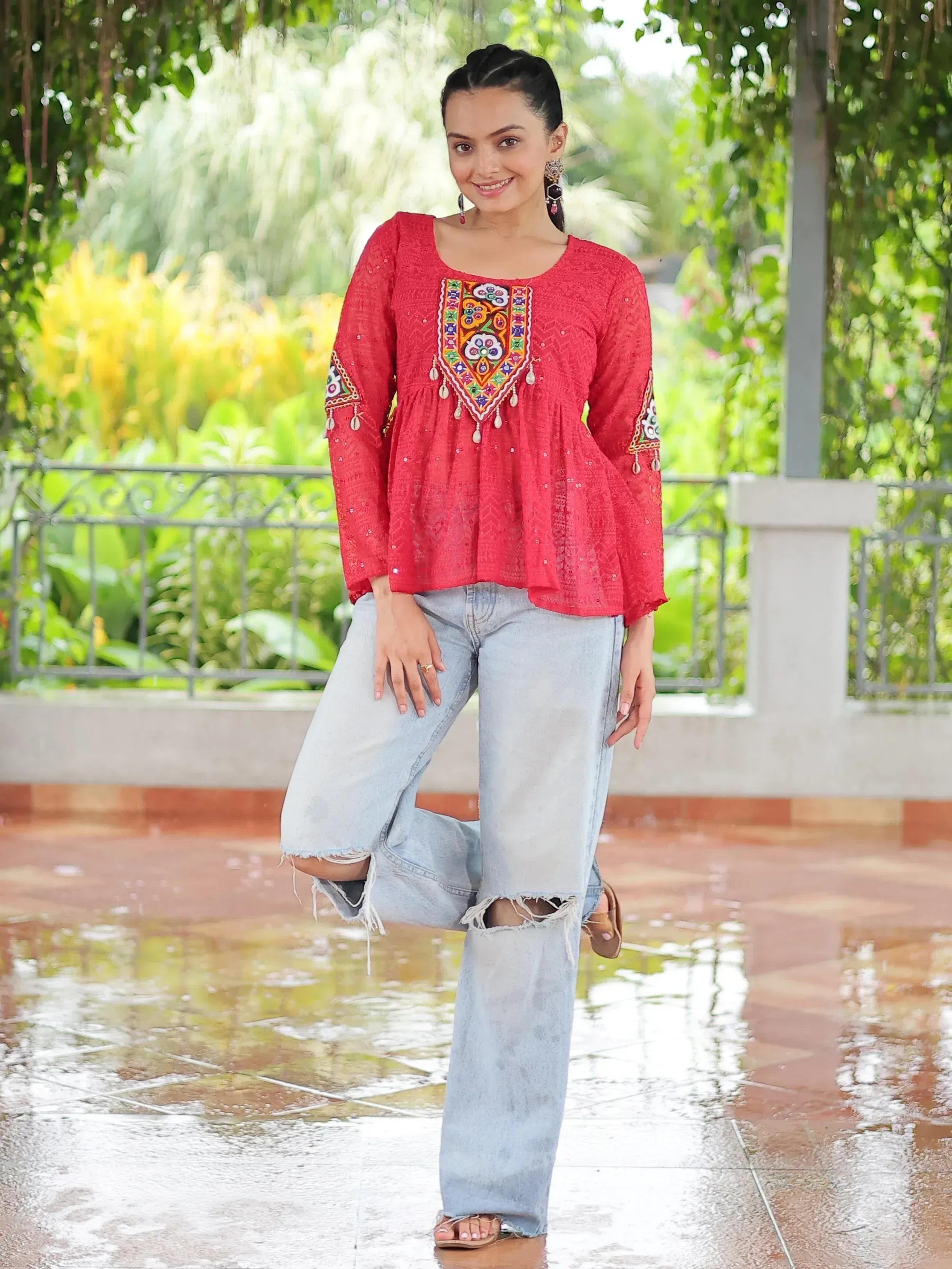 Red embroidered ethnic top with floral motifs, paired with ripped jeans, styled for casual wear.