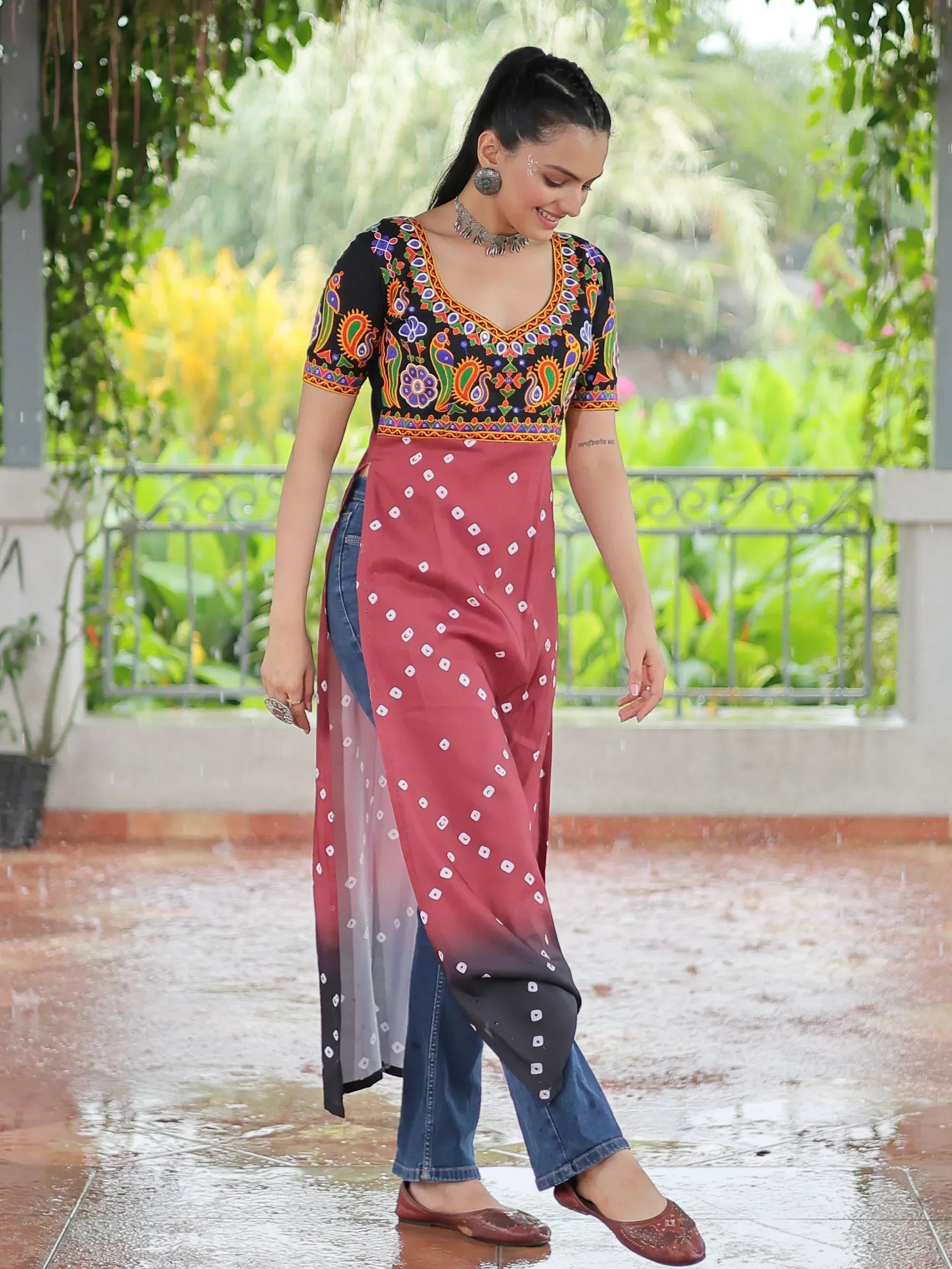 Woman in embroidered black top with colorful paisley, red bandhani dhoti pants, and denim jeans, styled for ethnic wear.