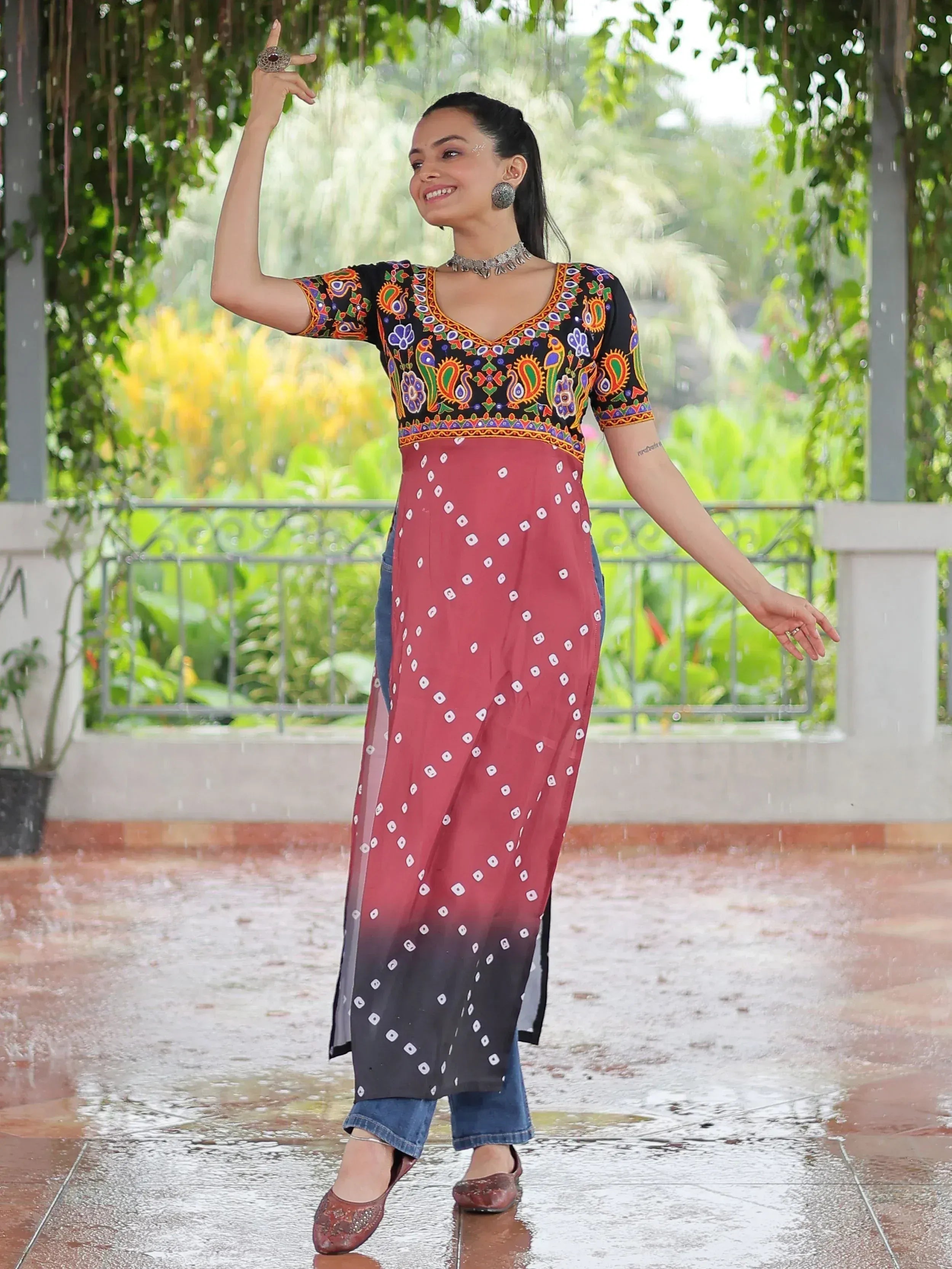 Woman in colorful embroidered kurta with bandhani print, paired with jeans, dancing in rain