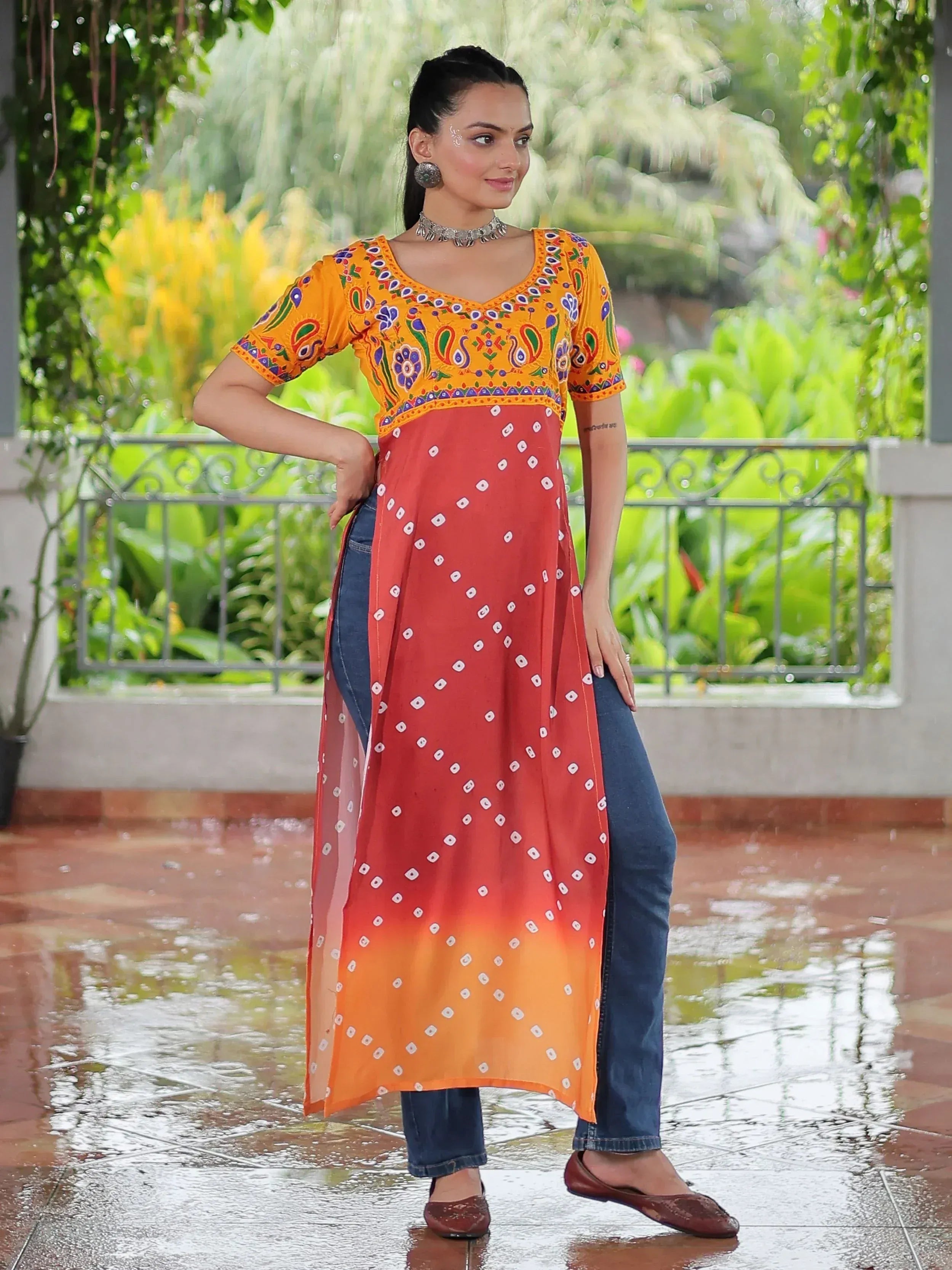 Woman wearing colorful embroidered ethnic kurti with bandhani print, paired with jeans, in garden setting