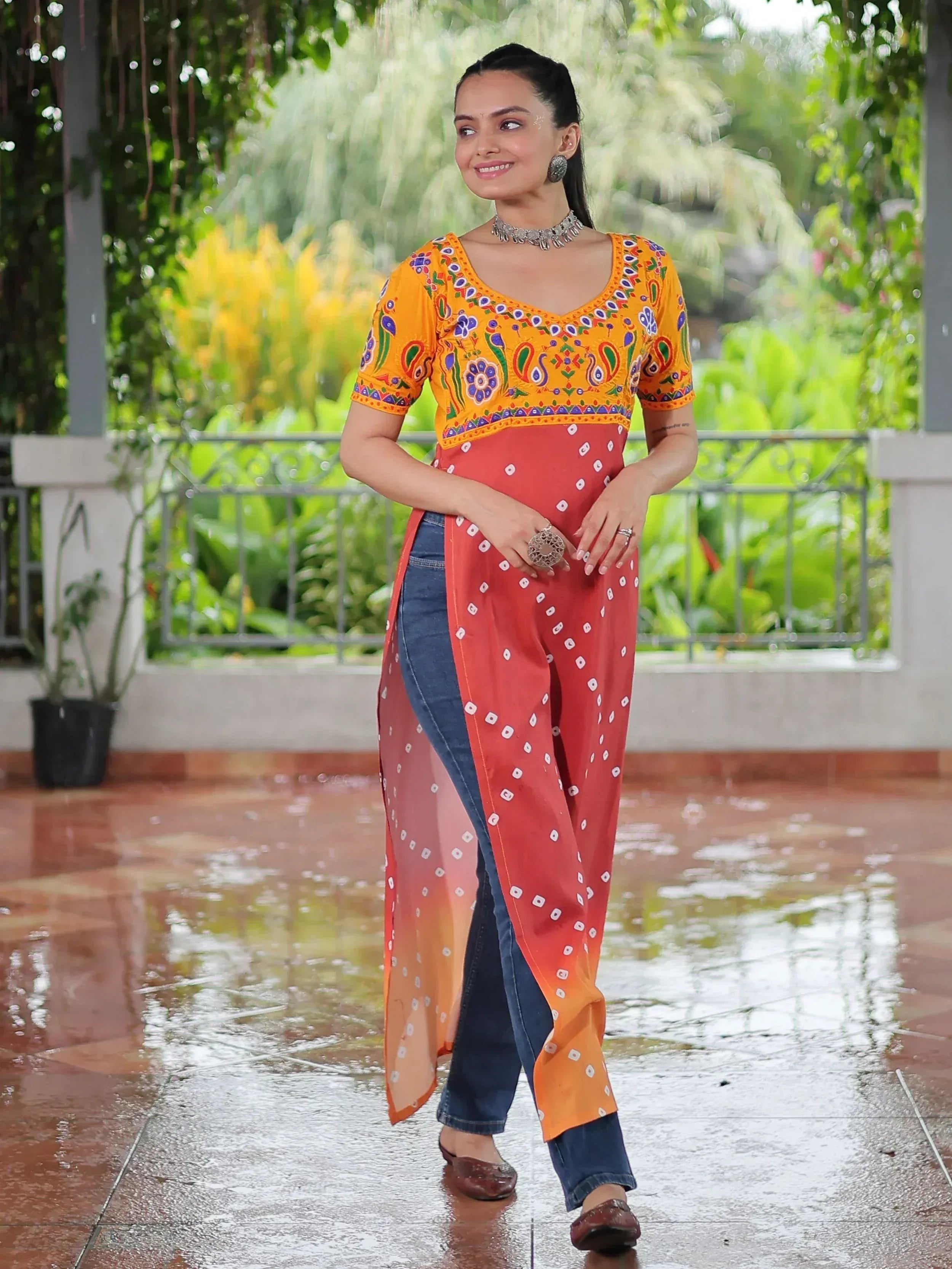 Woman in vibrant yellow embroidered top with red bandhani drape over jeans, ethnic Indian wear