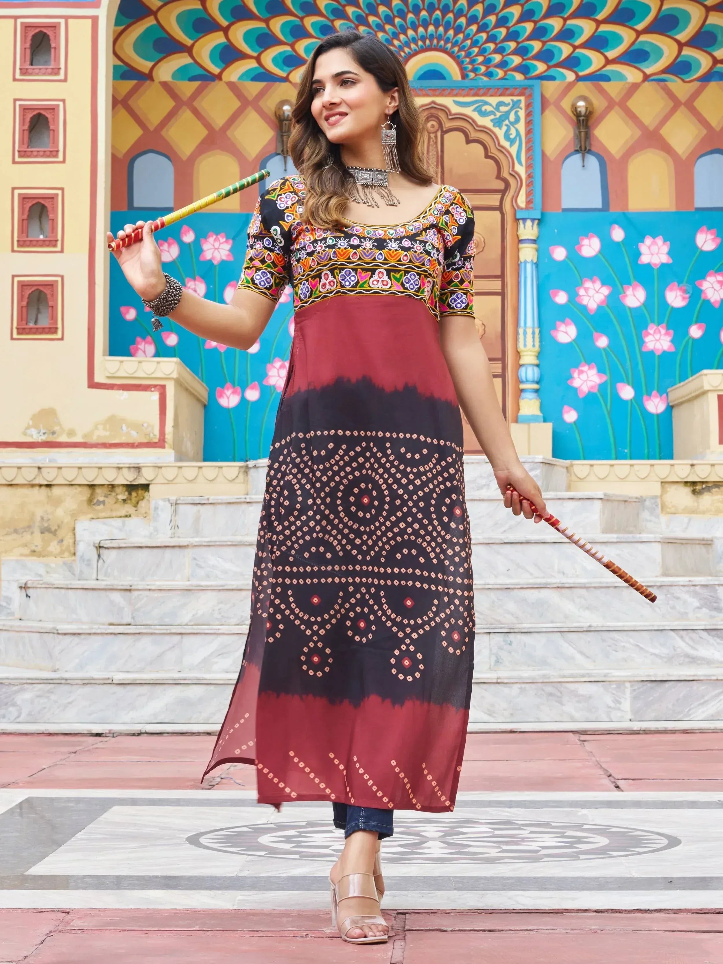 Woman in embroidered ethnic kurta with dandiya sticks, colorful Indian palace backdrop