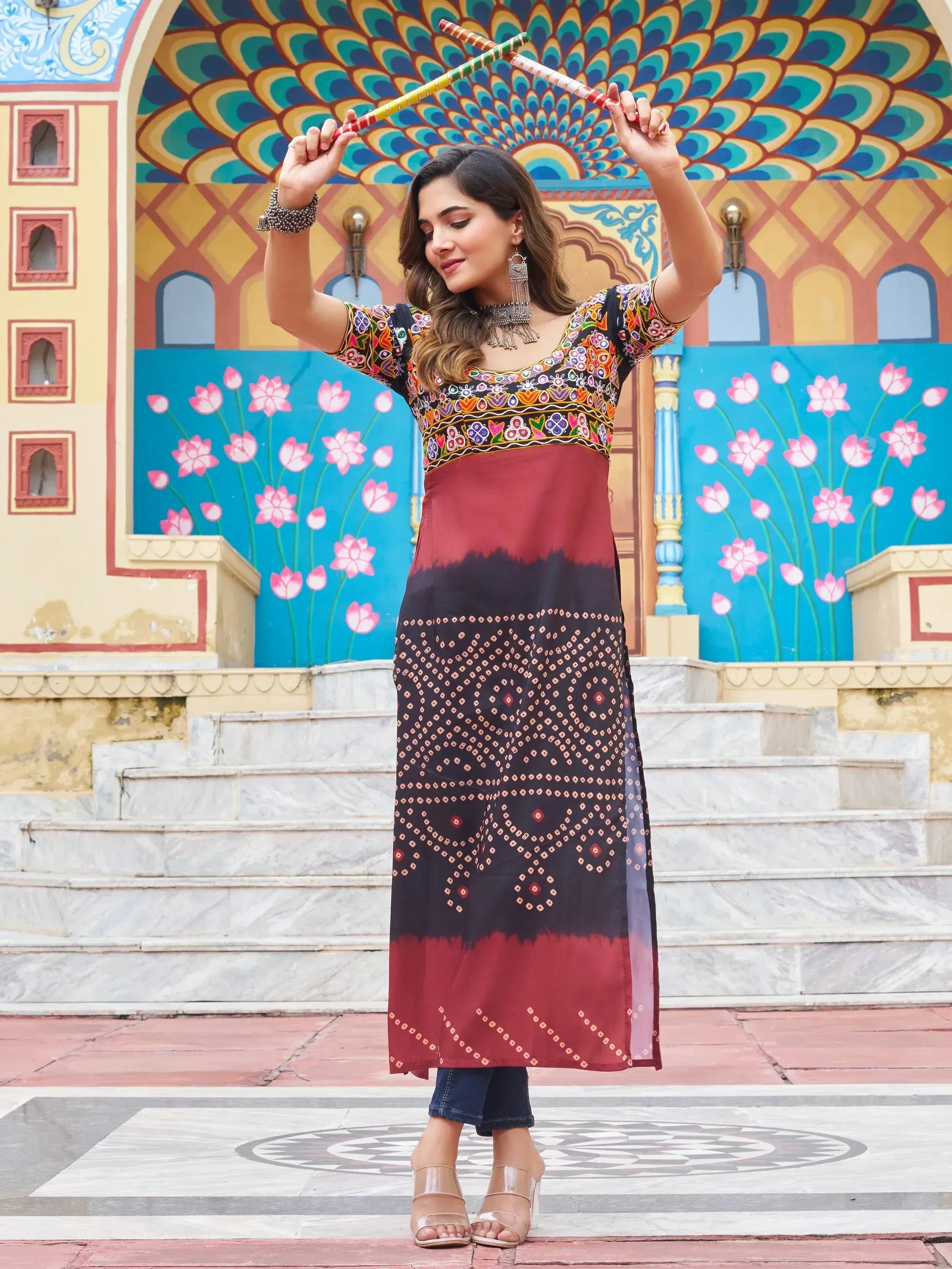 Woman in embroidered ethnic kurti with dandiya sticks, colorful peacock mural background