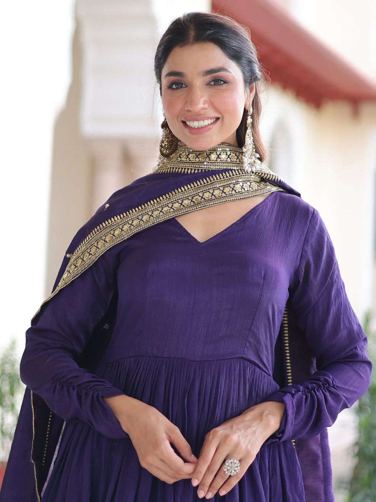 Woman wearing a purple designer Anarkali suit with gold embroidered border and ethnic jewelry