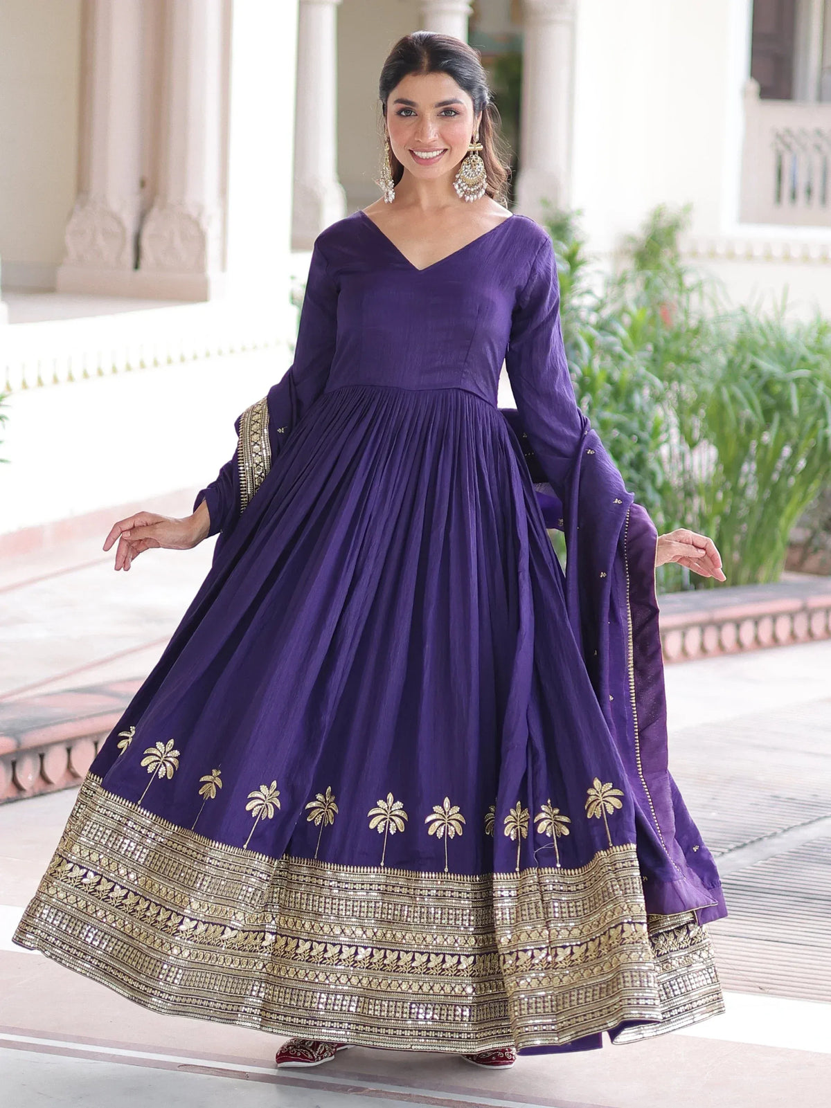 Woman wearing a purple ethnic gown with gold embroidery and matching dupatta.