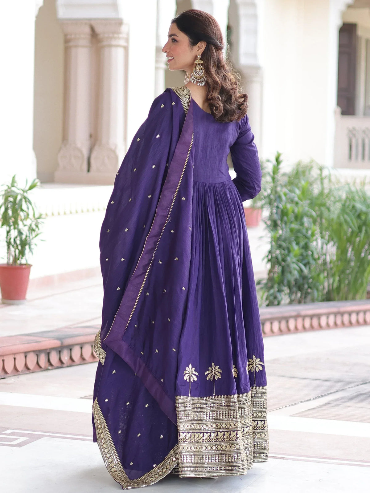 Woman in a purple Indian ethnic gown with gold embroidery and matching dupatta.