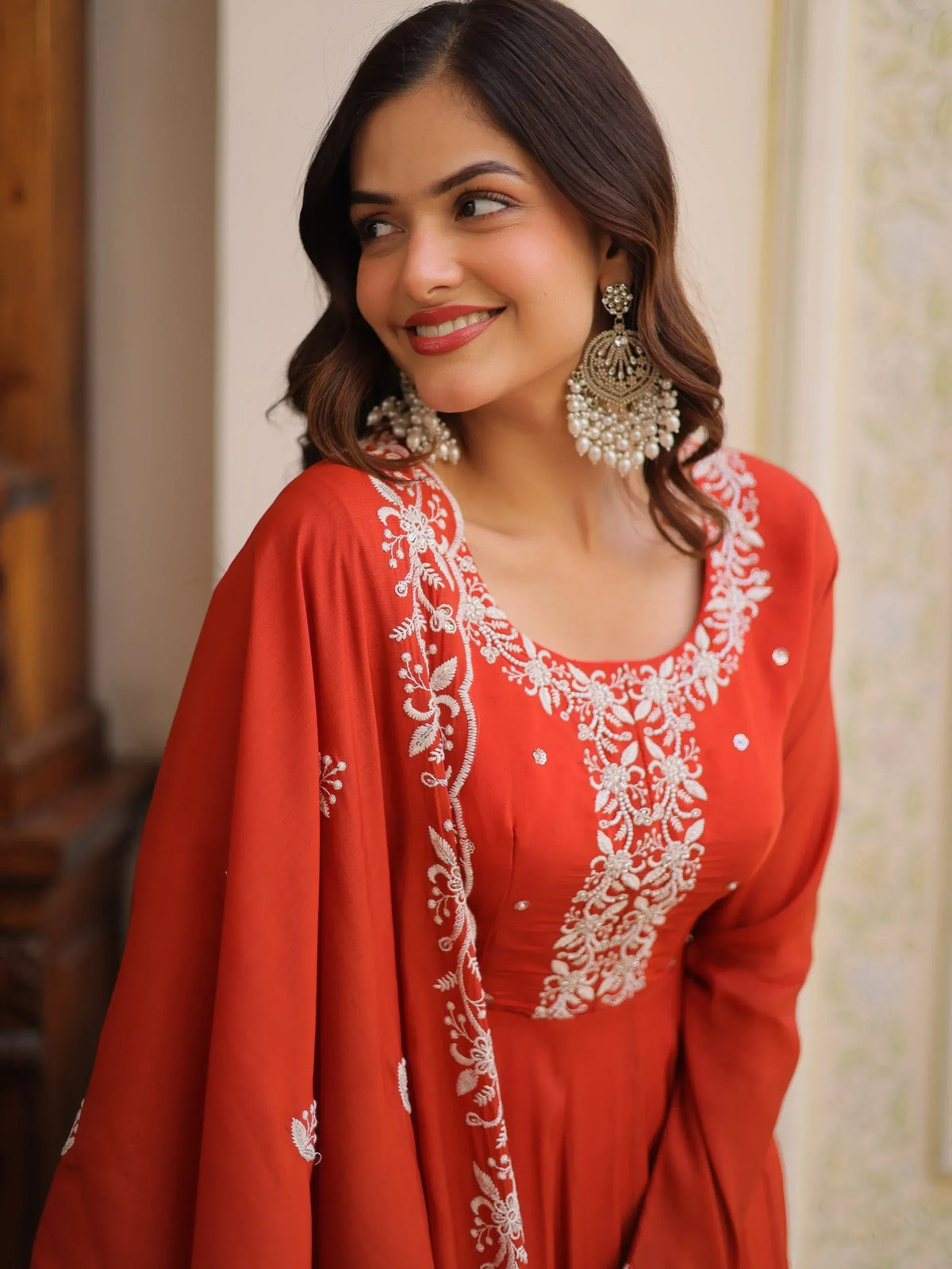 Woman wearing a red Indian ethnic salwar kameez with white floral embroidery and pearl earrings