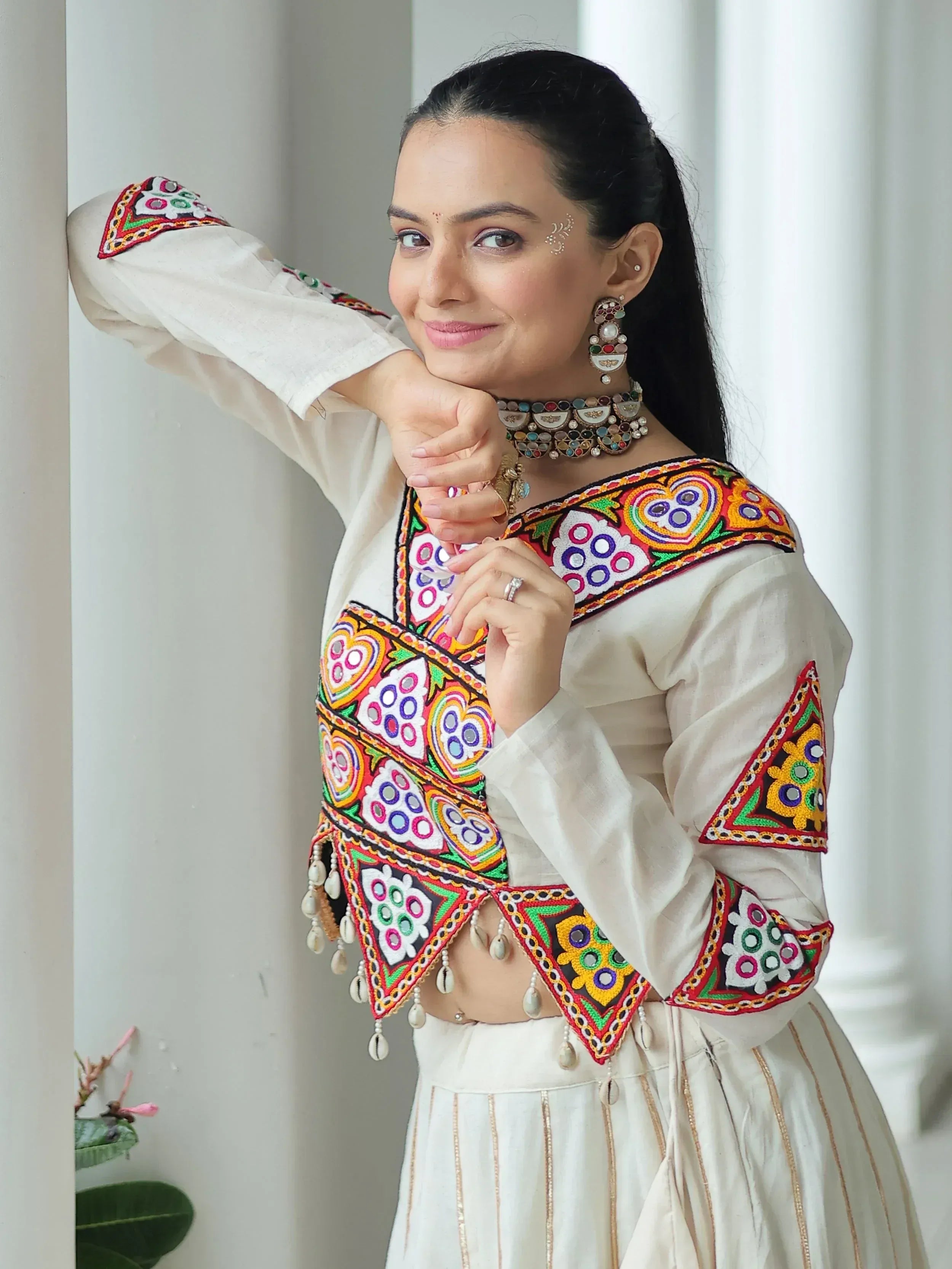 White embroidered ethnic top with colorful mirror work and tassels, paired with matching skirt