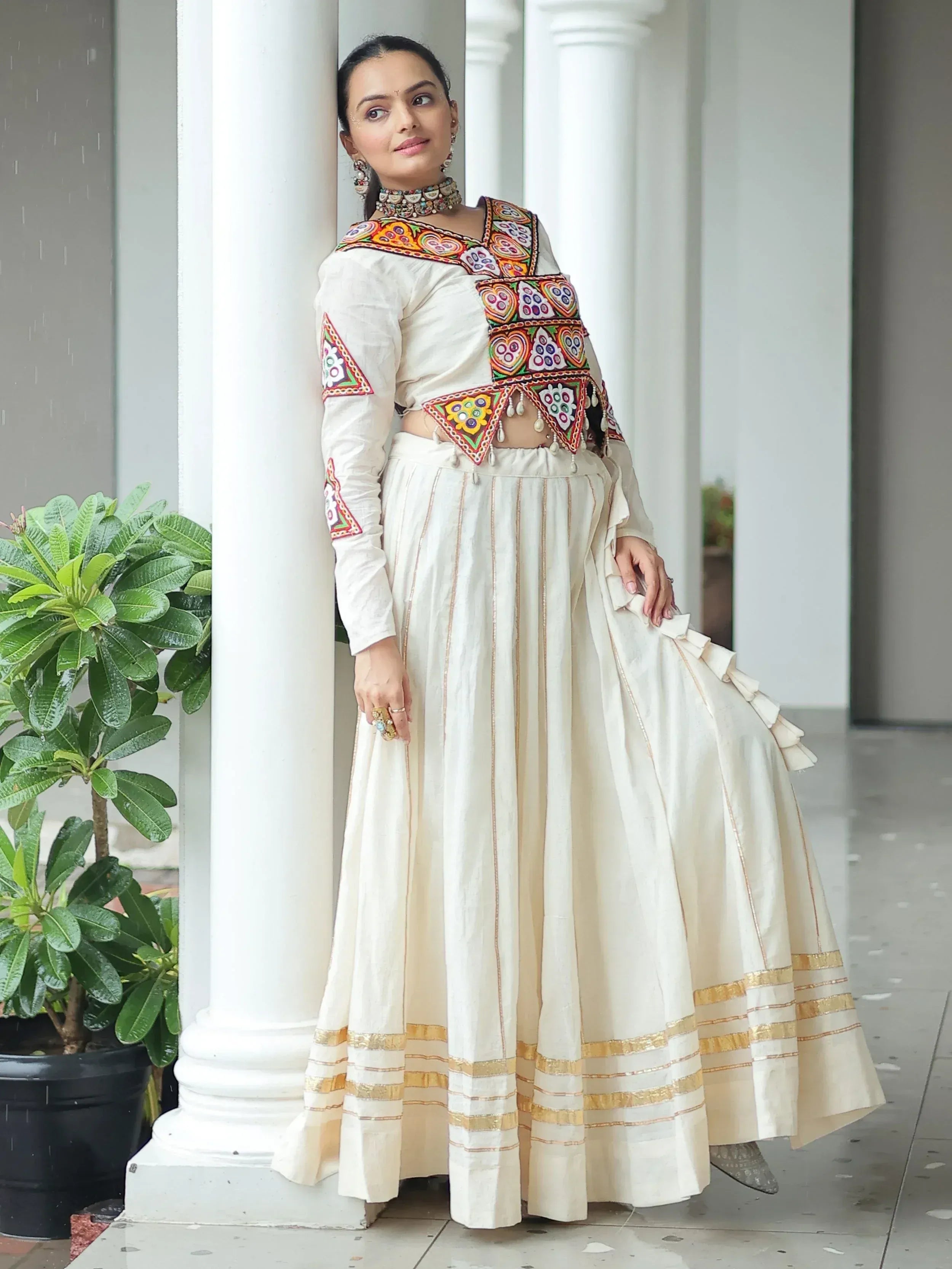 White embroidered lehenga choli with colorful mirror work, gold trim, and ruffled skirt for Indian ethnic wear