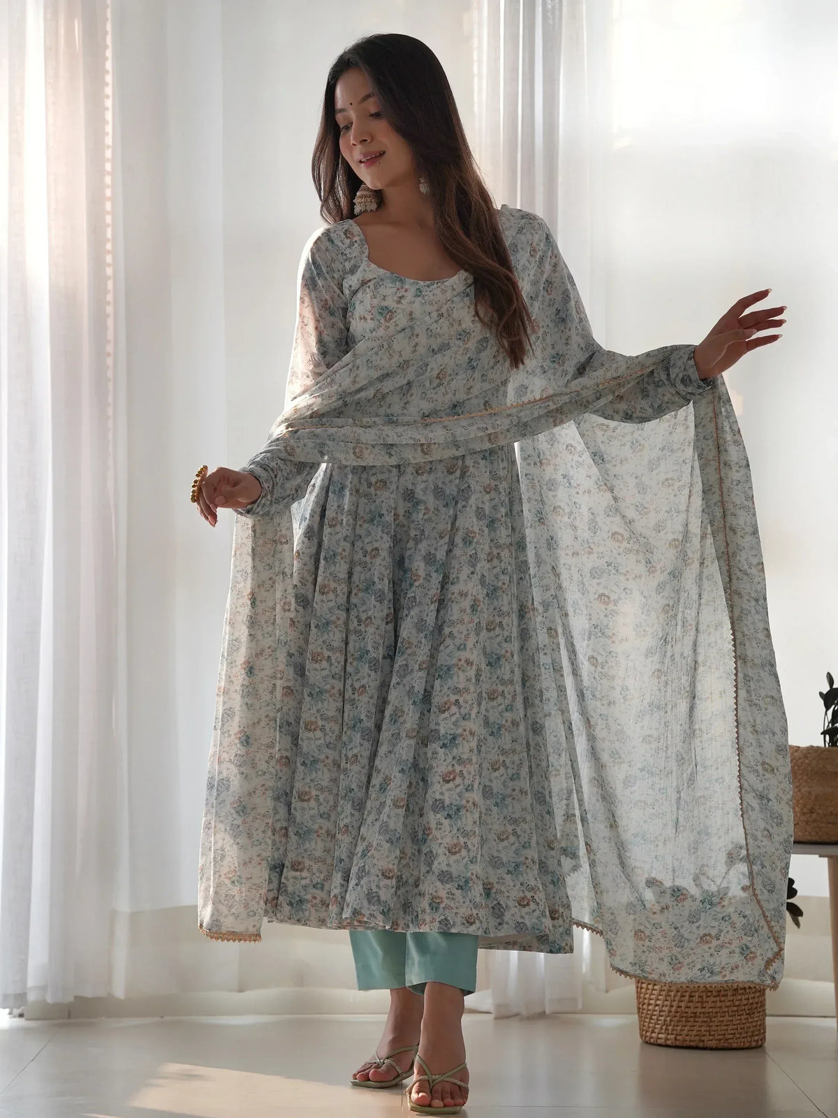 Woman in floral print Indian ethnic anarkali suit with matching dupatta, light blue pants, and sandals