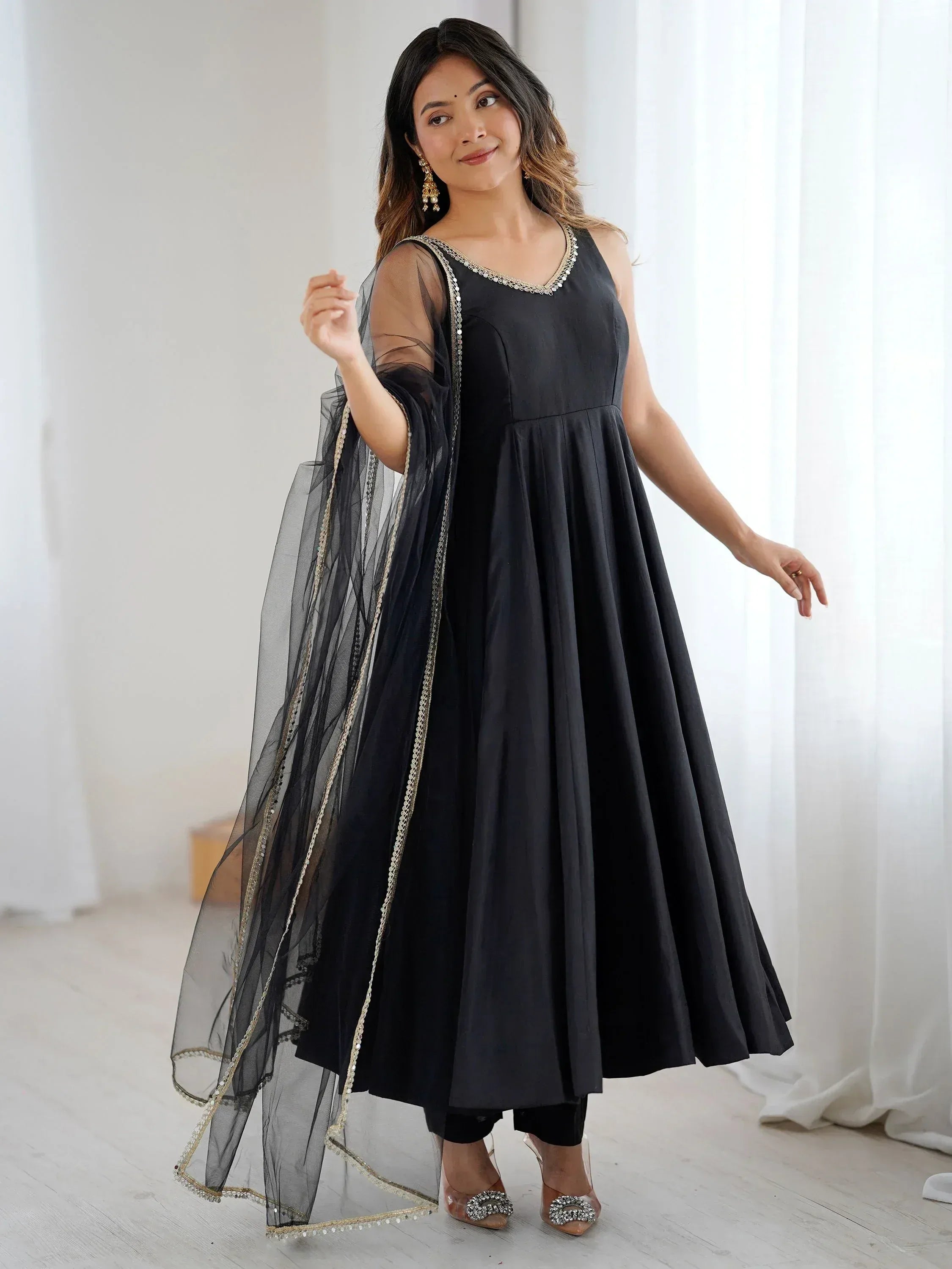Black ethnic gown with sheer dupatta, gold trim, and embellished neckline for festive occasions