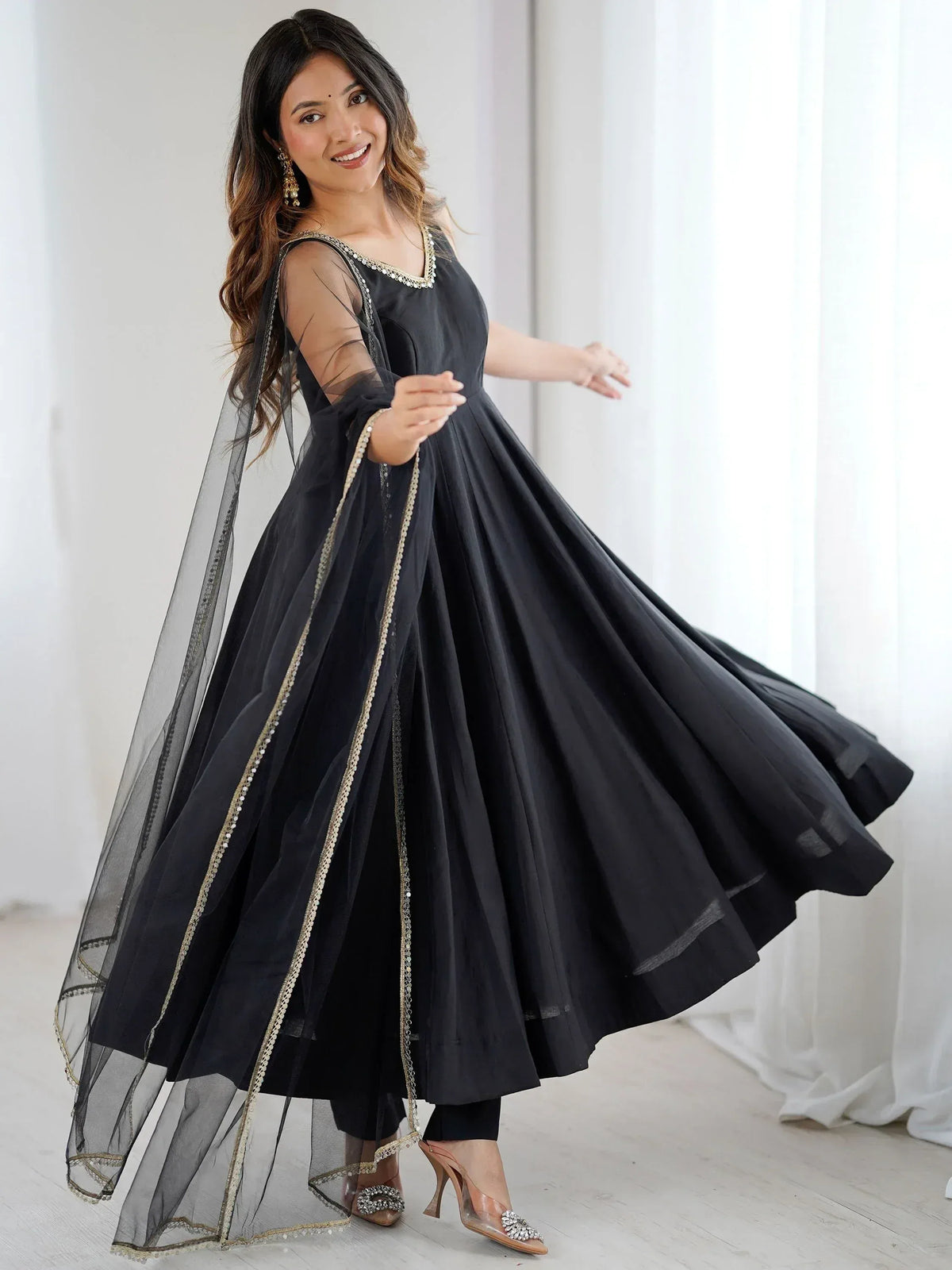 Black ethnic gown with gold trim, sheer dupatta, and embellished neckline for festive occasions