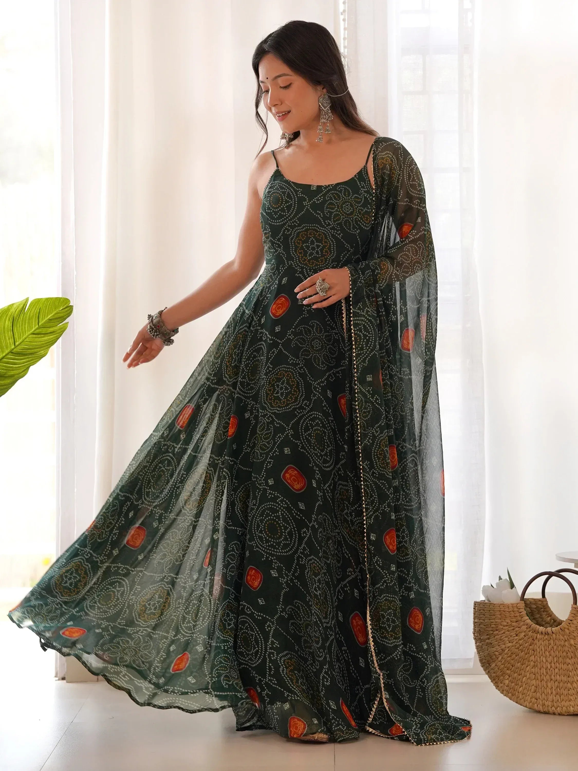 Woman wearing dark green designer ethnic gown with orange accents and traditional jewelry