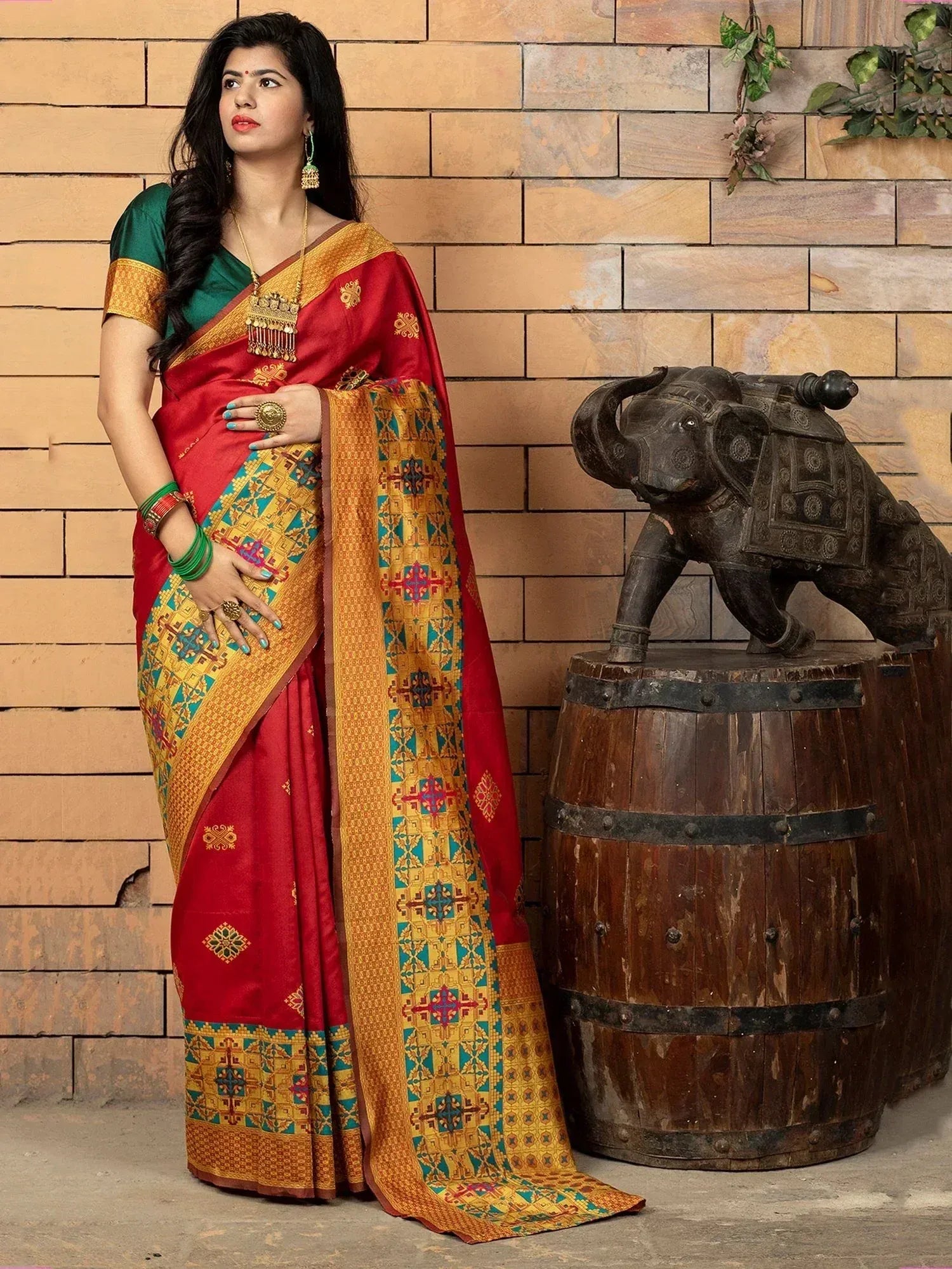 Red and gold designer saree with intricate geometric patterns, paired with green blouse, ideal for Indian ethnic occasions.