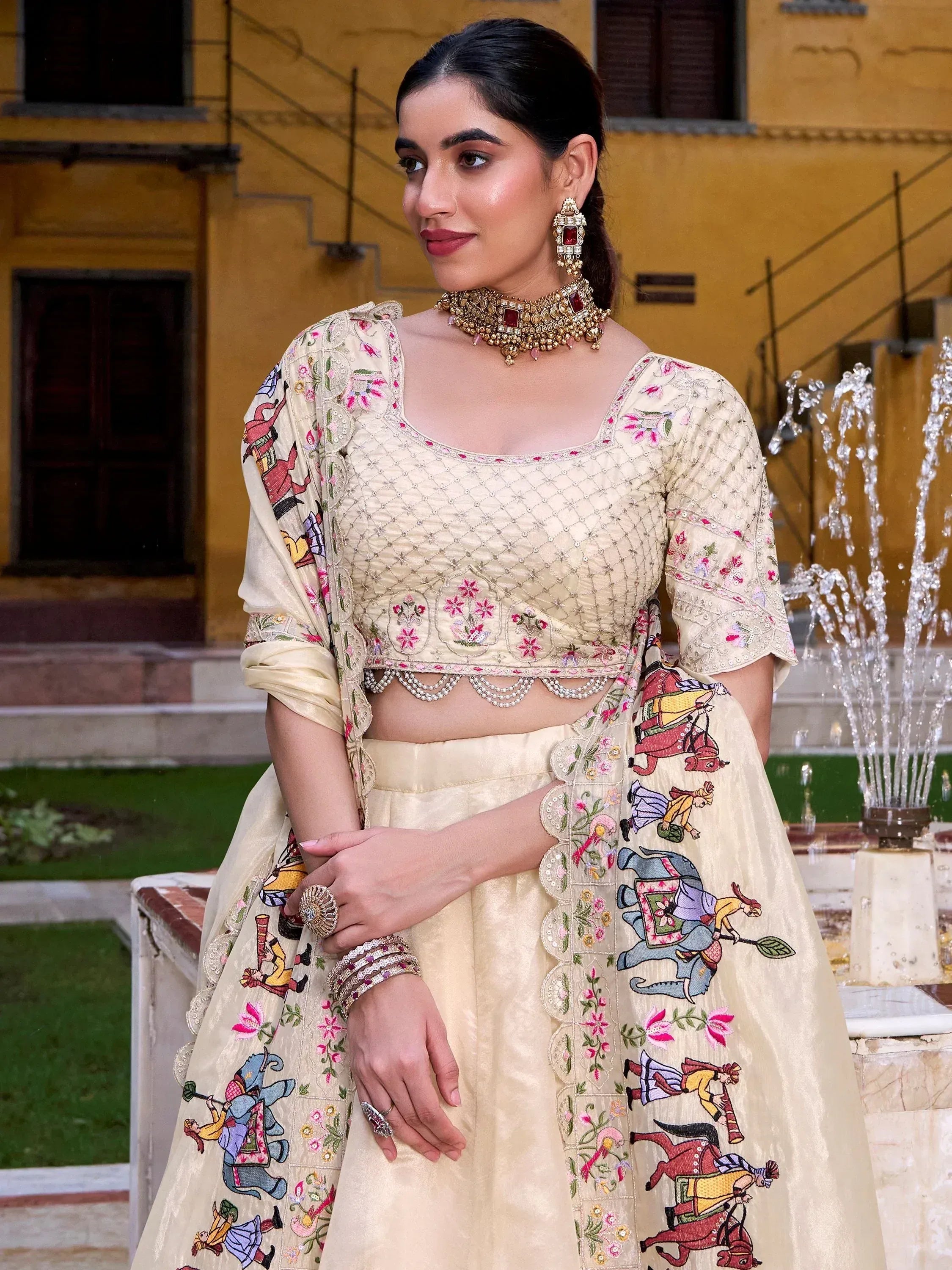 Cream embroidered lehenga choli with floral and elephant motifs, paired with traditional jewelry