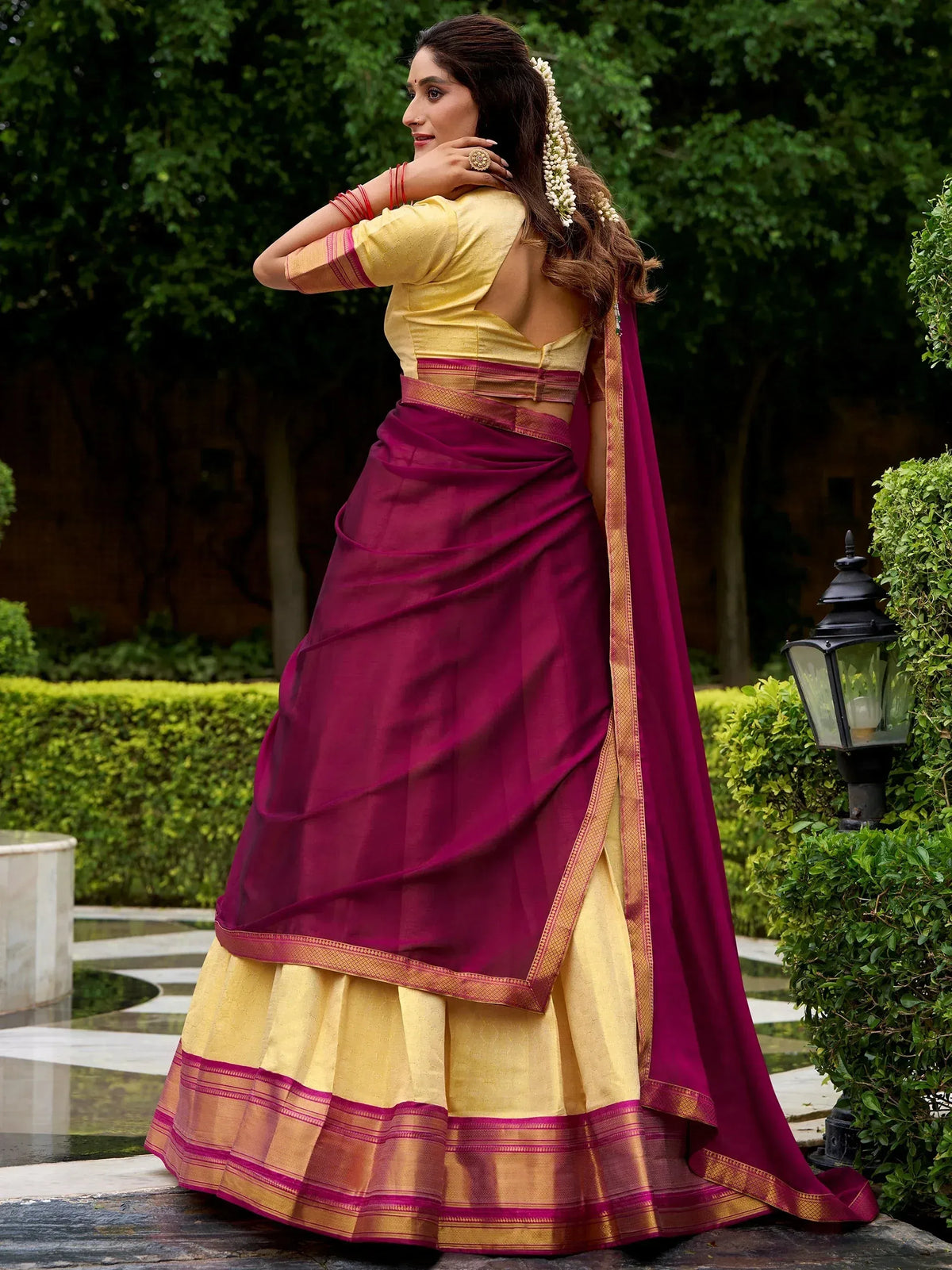 Woman in maroon and yellow designer lehenga choli with floral hair accessories, garden setting