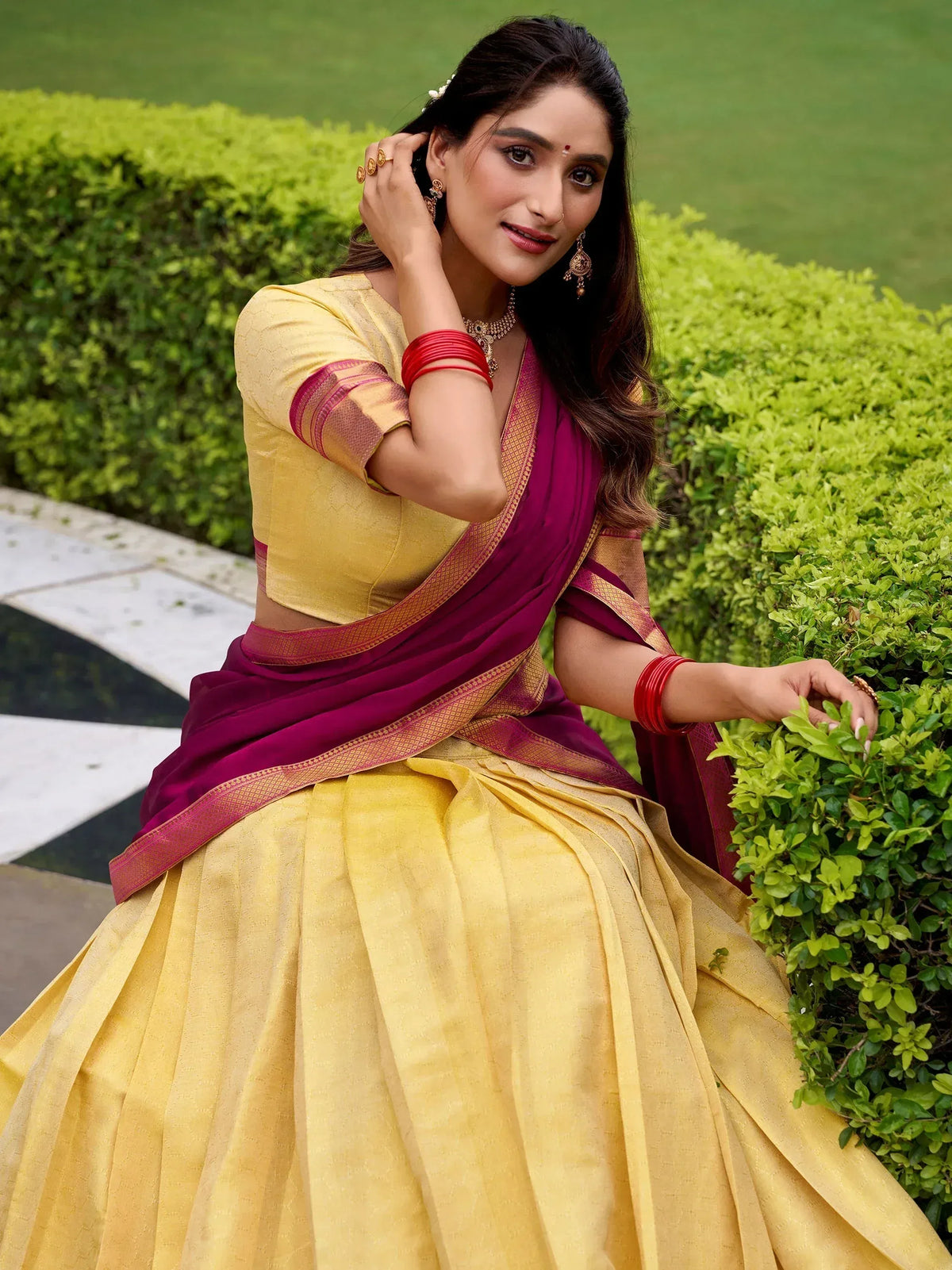 Woman in yellow and maroon designer lehenga choli with gold border, perfect for Indian ethnic occasions