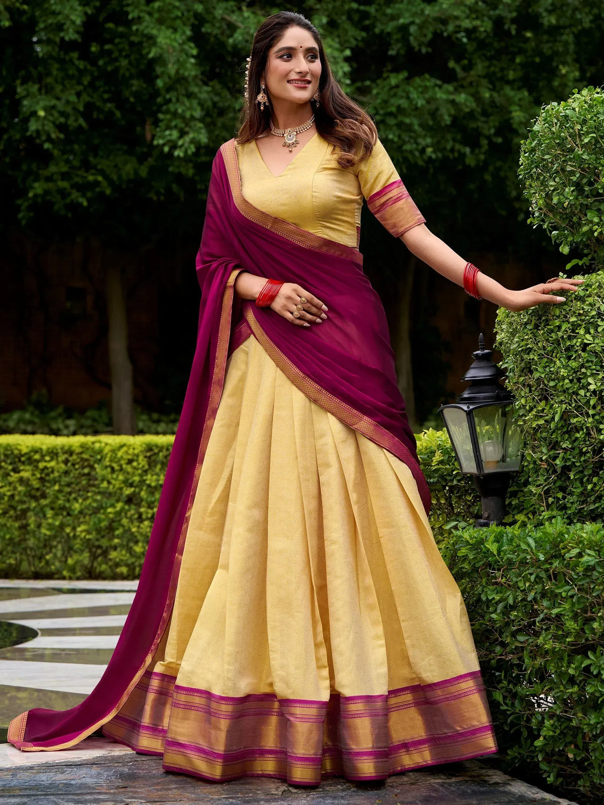 Woman in yellow and maroon designer lehenga choli with gold border, perfect for Indian ethnic wear occasions