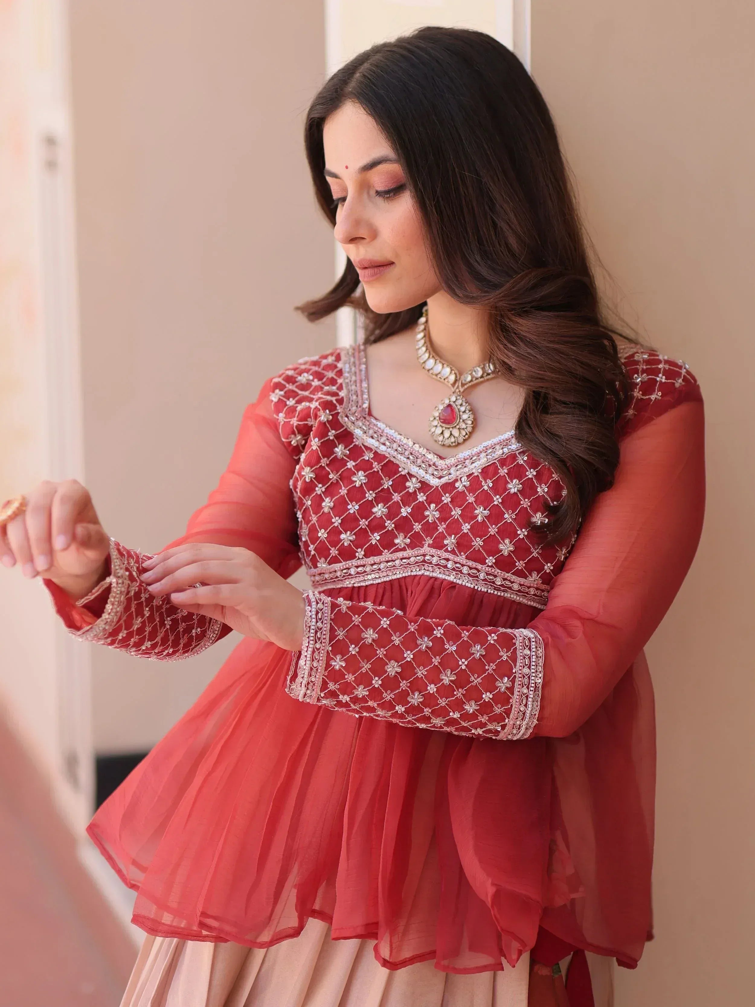 Red embroidered ethnic gown with sheer sleeves and floral detailing, paired with traditional jewelry